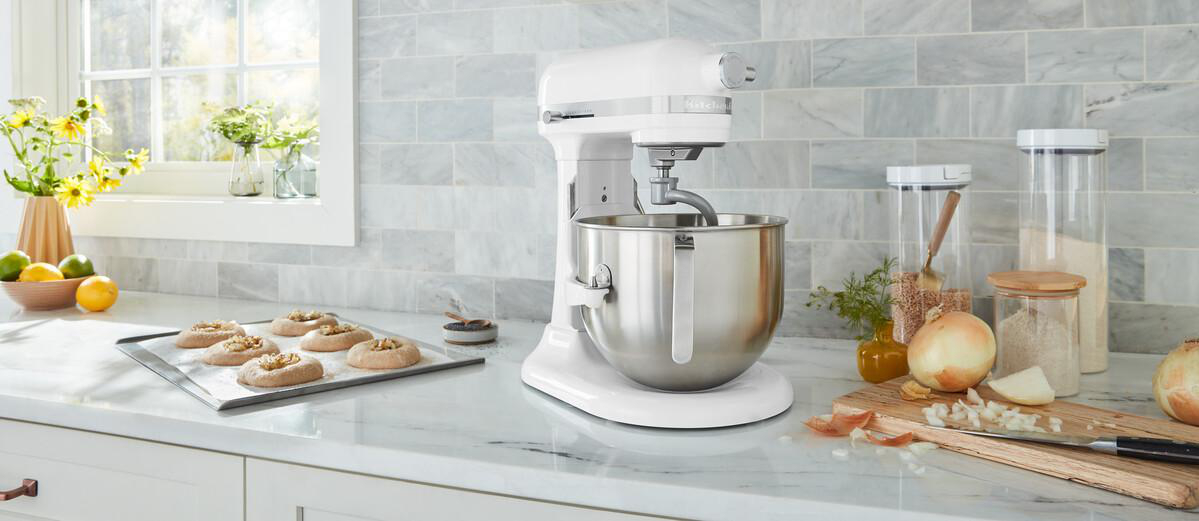 Weißer KitchenAid Mixer auf Marmorplatte mit Gebäck und Zutaten.
