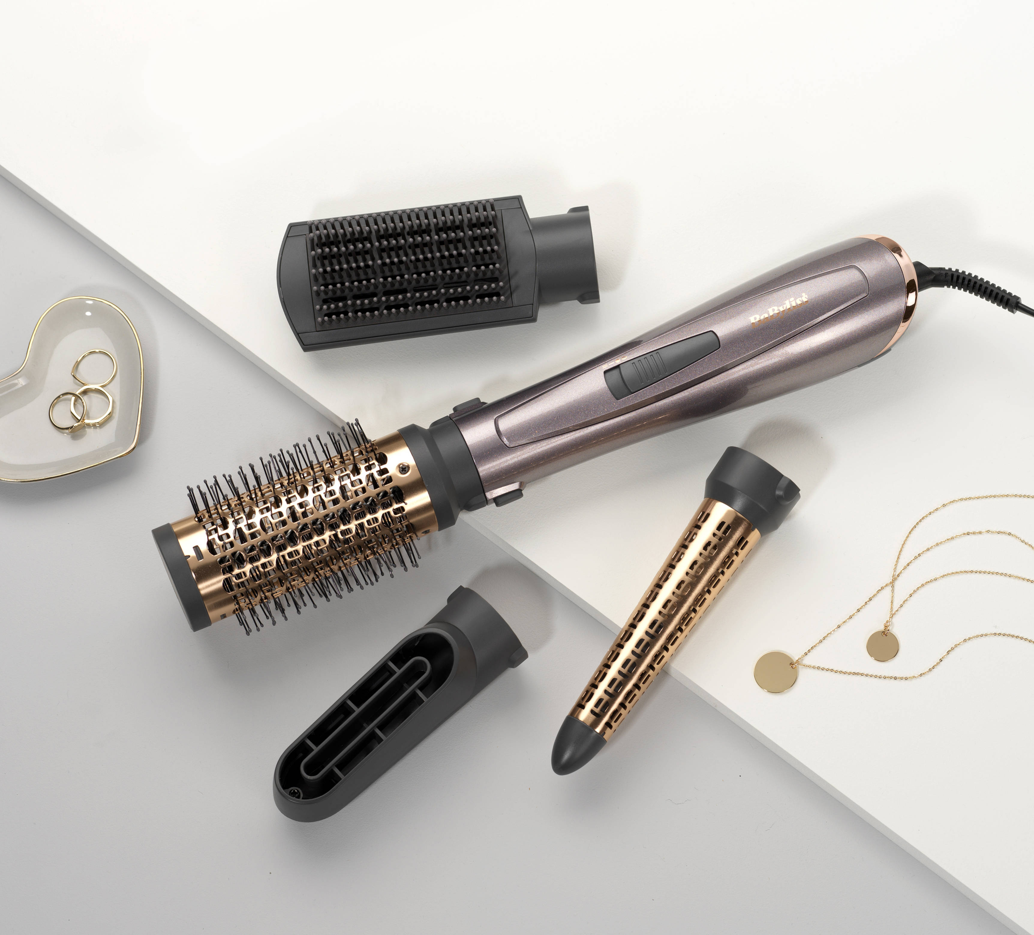 Des outils de coiffure, dont une brosse et un sèche-cheveux, sont présentés sur fond blanc.
