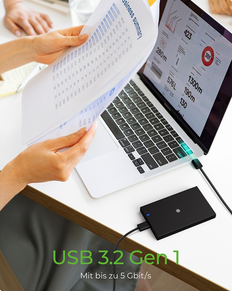 Person arbeitet an einem Laptop neben einer schwarzen externen Festplatte, USB 3.2 Gen 1, auf einem Schreibtisch.