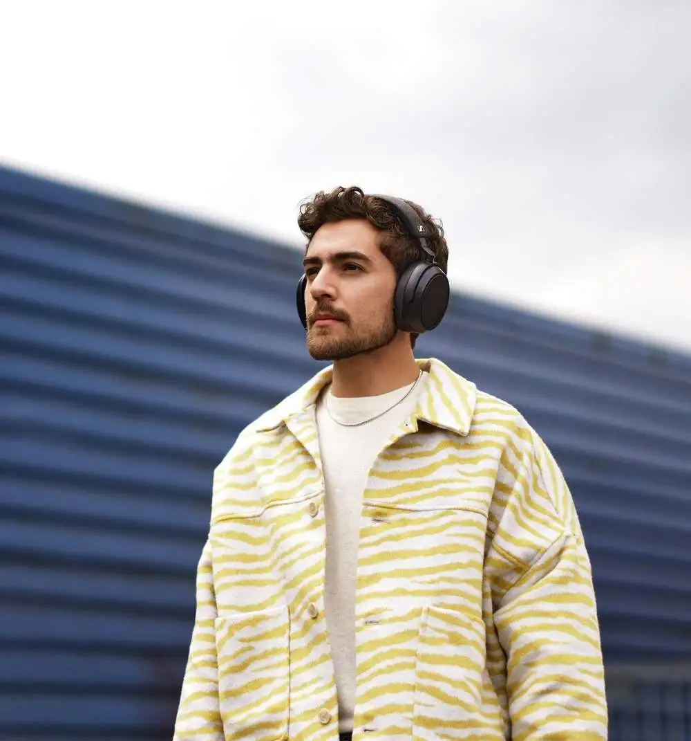 Un homme en veste jaune et casque regarde hors champ contre un mur à rayures bleues.