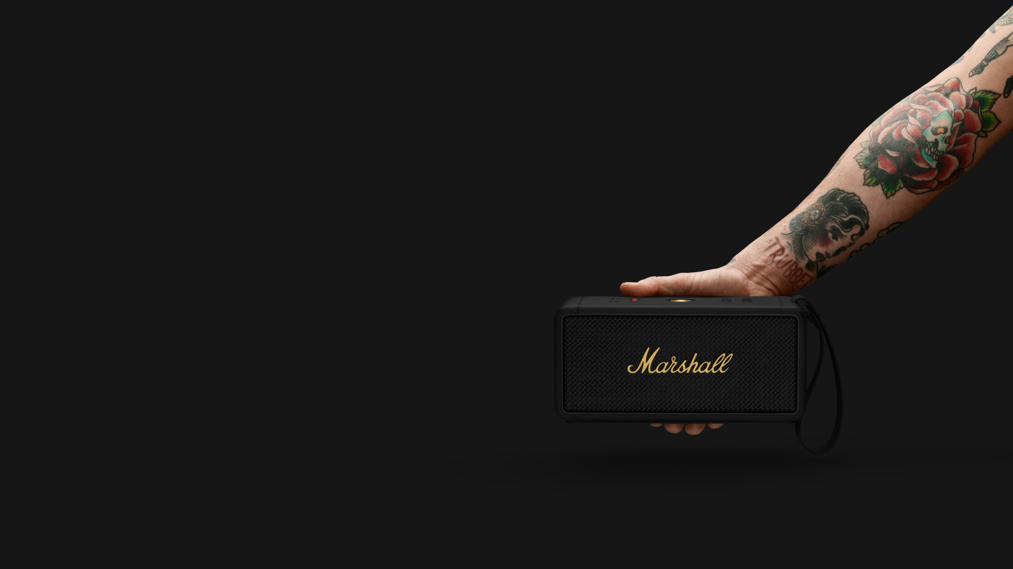 Hand hält einen Marshall-Lautsprecher. Arm hat Tattoos. Schwarzer Hintergrund.