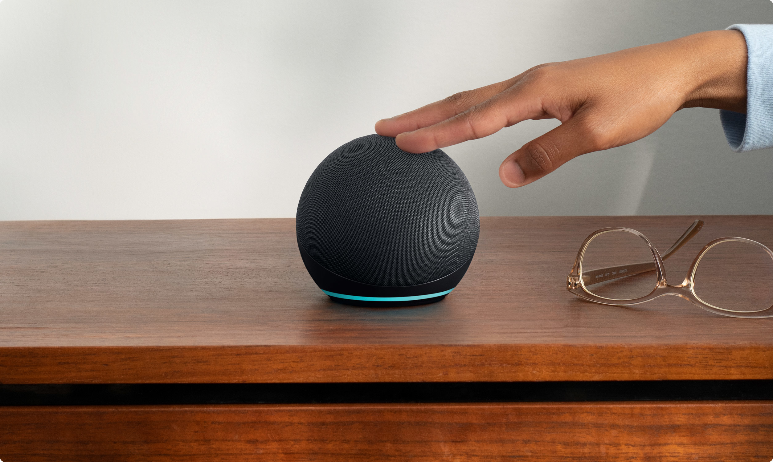 Une main touchant un haut-parleur intelligent noir sur du bois.