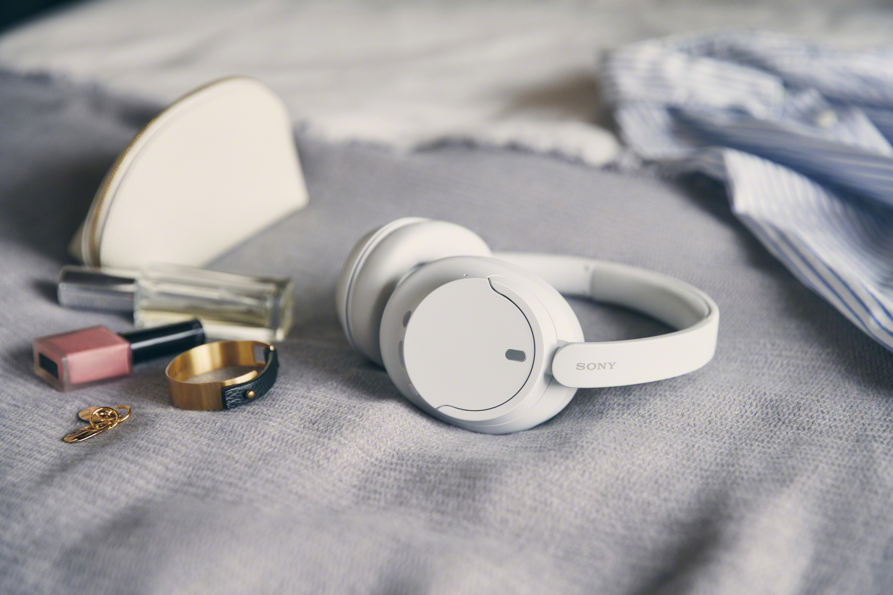 Casque blanc, trousse de maquillage, vernis à ongles, bagues et clés sur surface grise avec chemise bleue.
