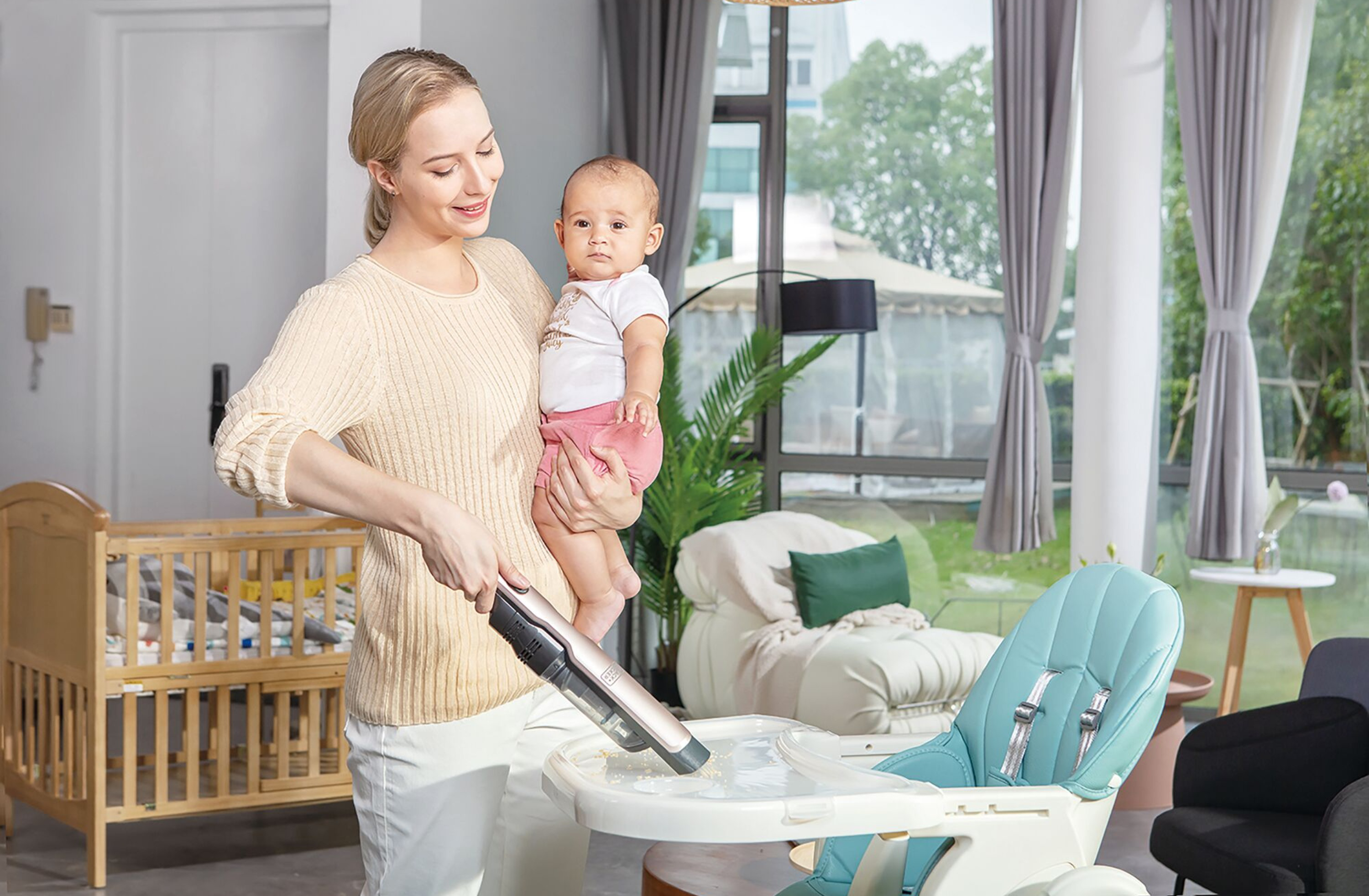 Frau hält Baby, reinigt Hochstuhl mit Staubsauger in einem Raum.