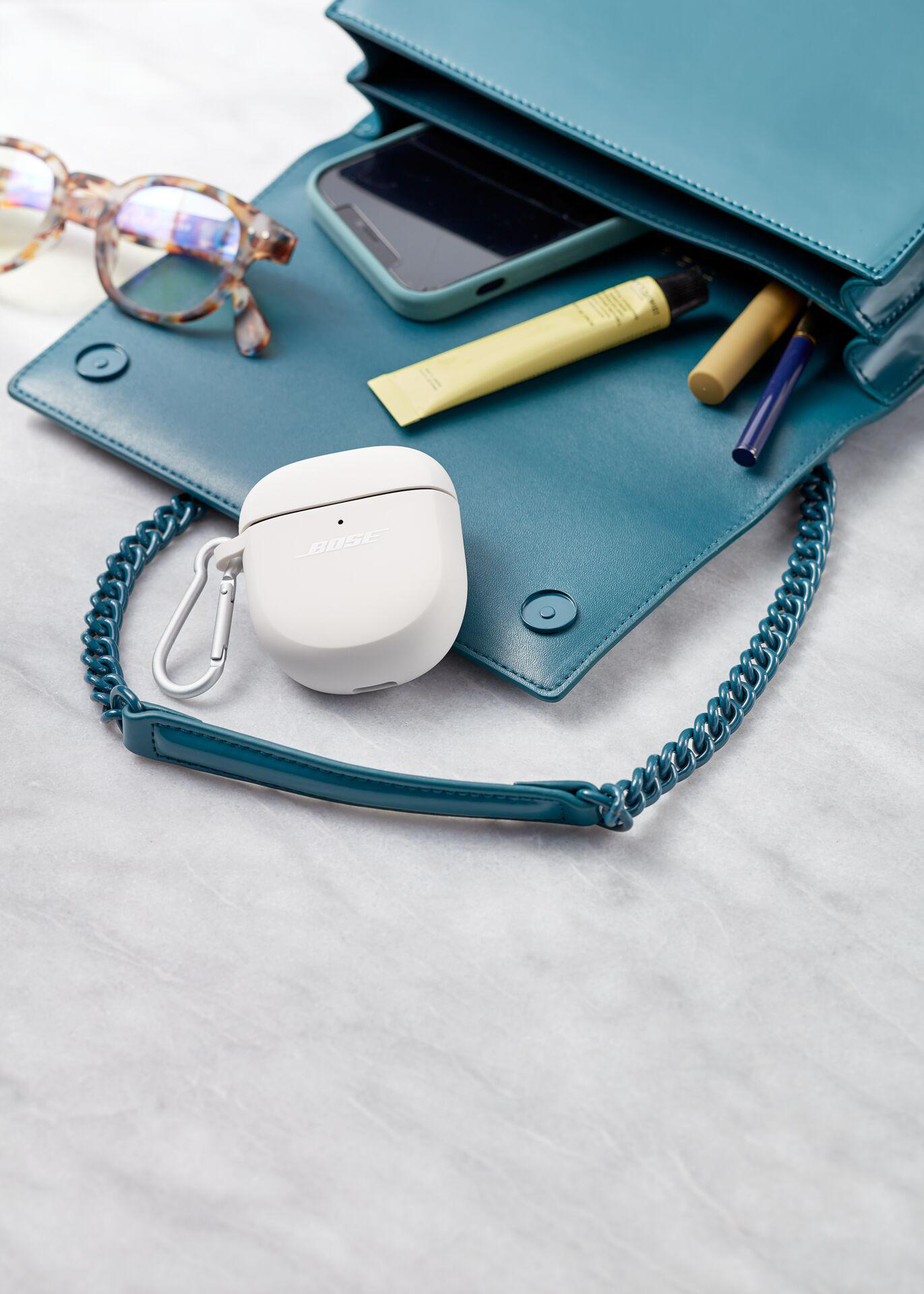 Türkisfarbene Handtasche mit Inhalt: Brille, Telefon, Kopfhörer, Make-up, auf heller Oberfläche.