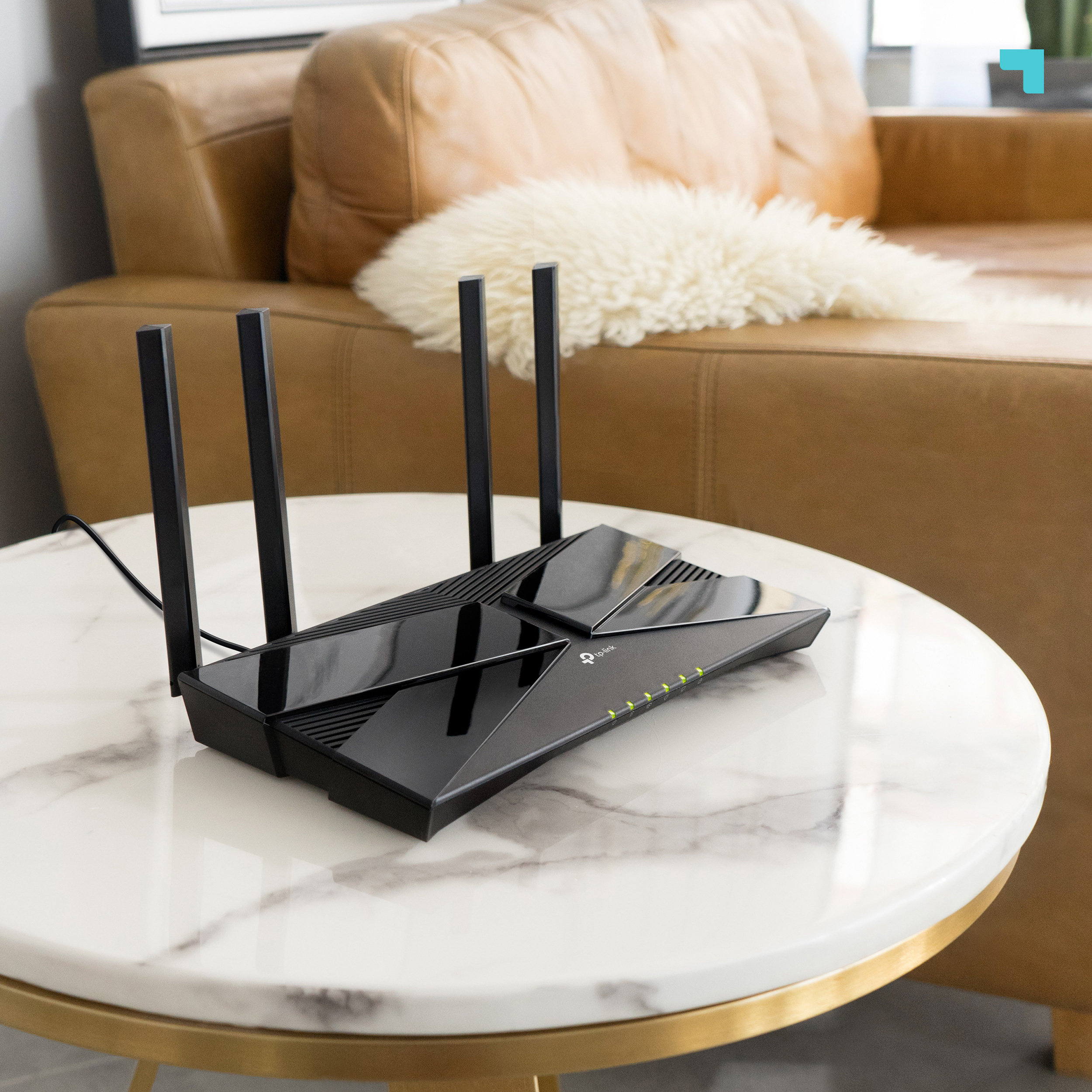 Router negro con antenas en mesa de mármol. Sofá marrón y piel blanca en el fondo.