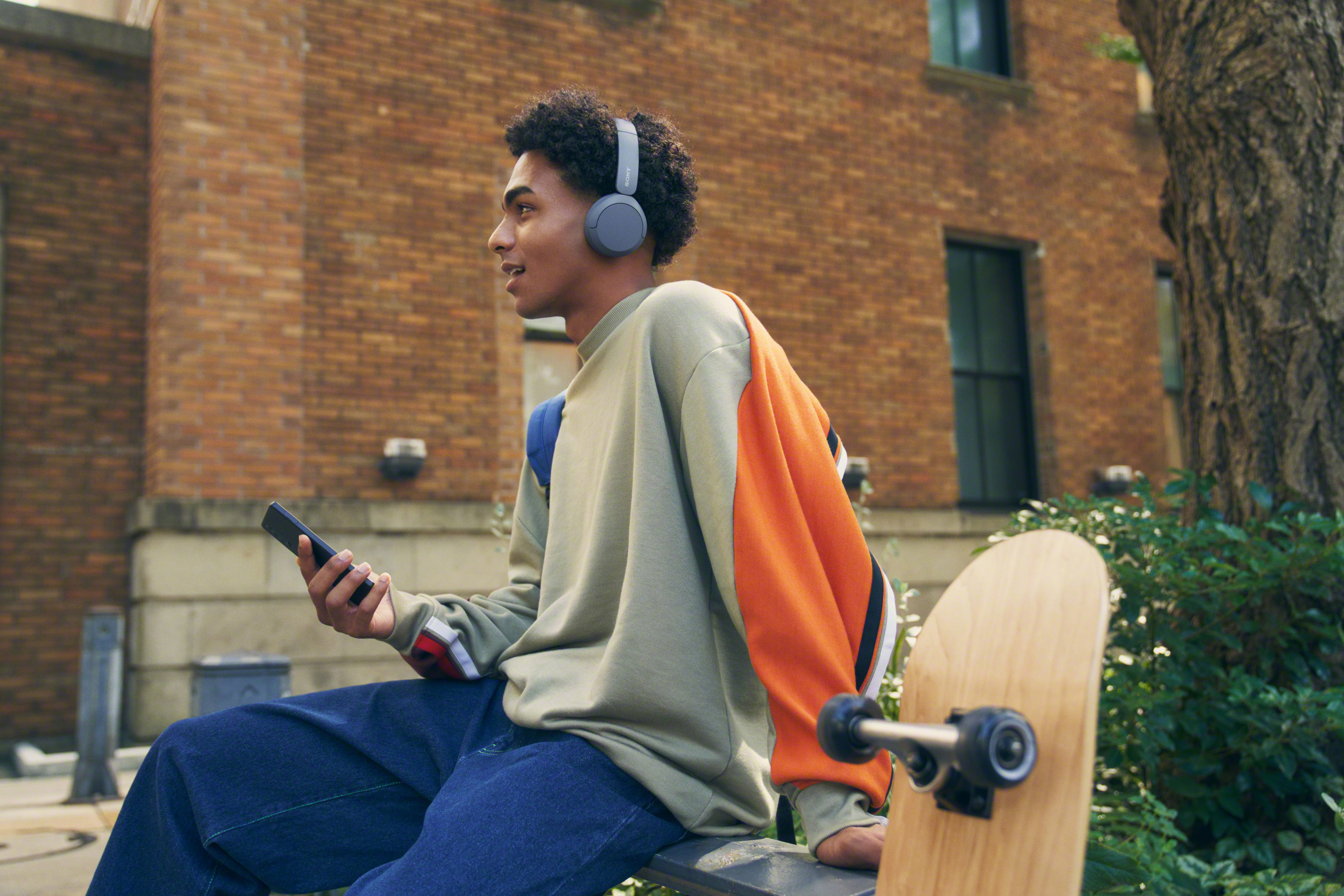 Un jeune homme avec un casque et un téléphone, assis sur un banc avec un skateboard.