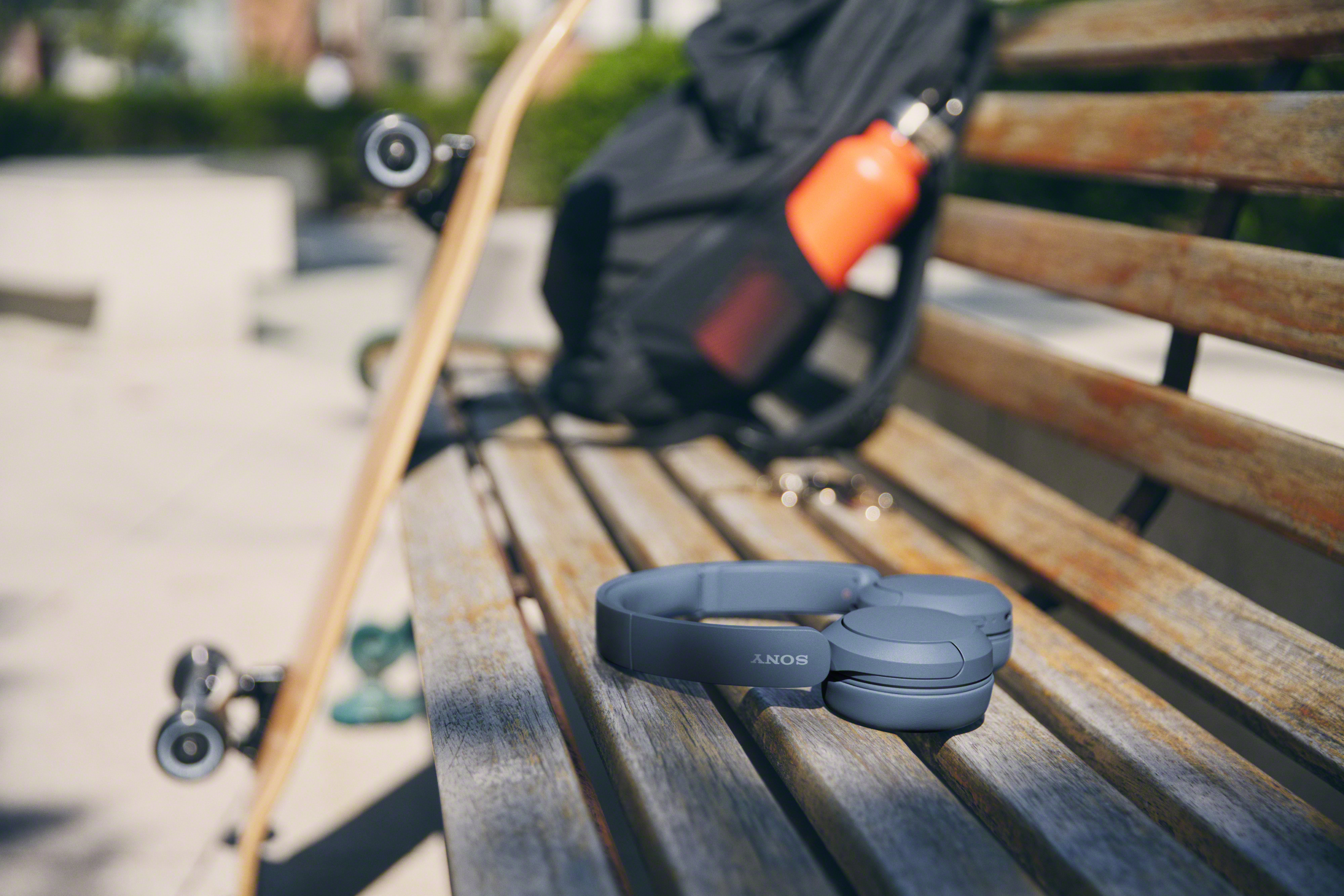 Casque sur un banc à côté d'un skateboard, d'un sac à dos et d'une bouteille d'eau orange.