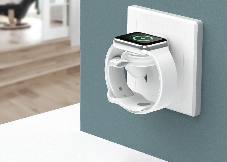 Fehér Apple Watch egy fali aljzatba dugott töltőn.