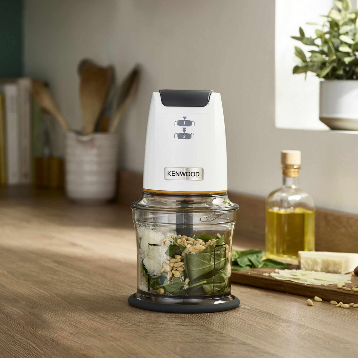 A white and orange Kenwood food processor with ingredients inside, on a wooden surface.