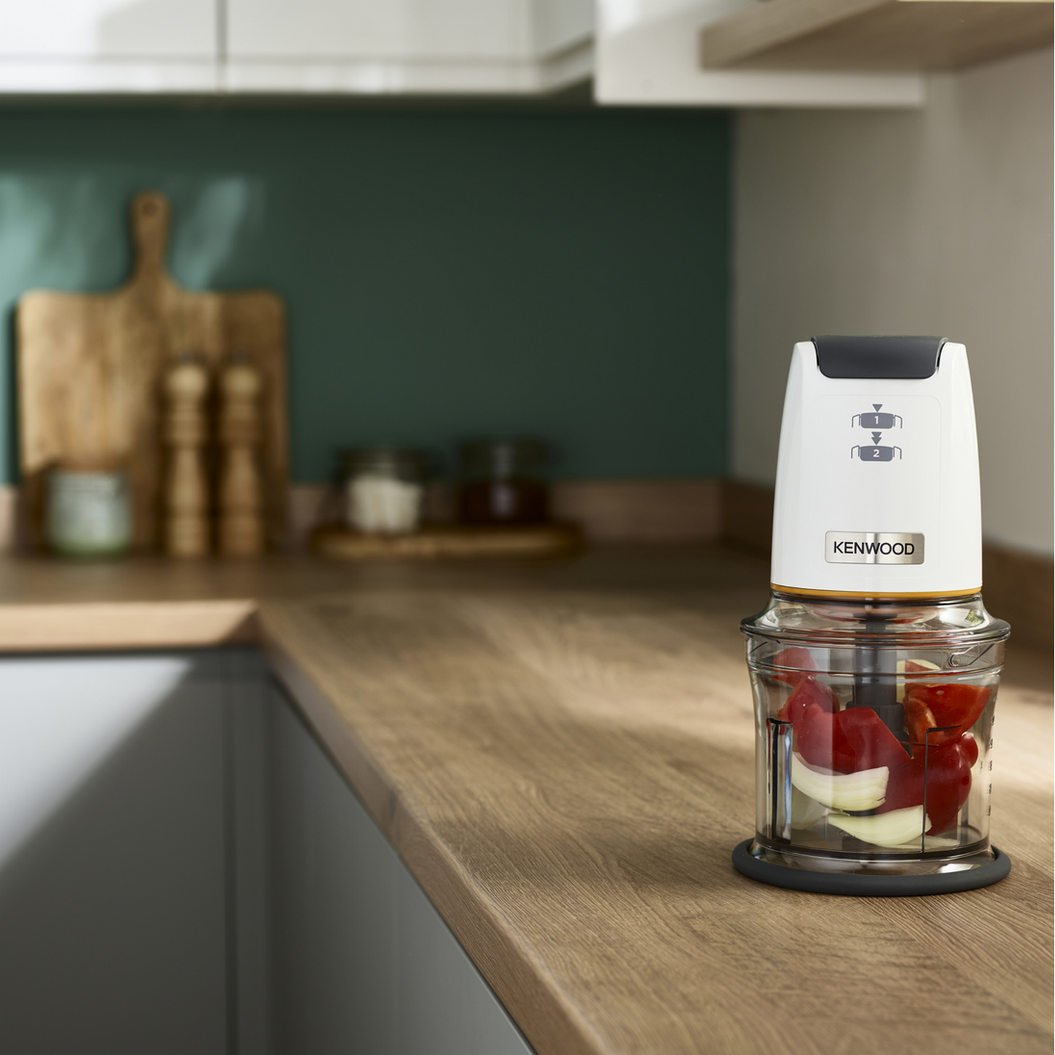 A Kenwood food chopper with red peppers and onions inside, on a wooden surface.