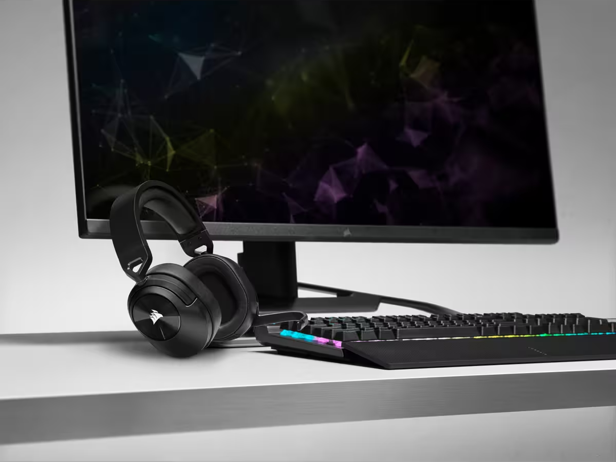 Casque et clavier noirs sur une surface blanche, avec un moniteur noir en arrière-plan.