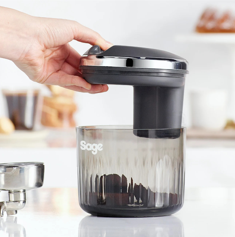 Hand entfernt den Mahlwerkaufsatz von einer Sage-Kaffeemühle mit transparentem Behälter.