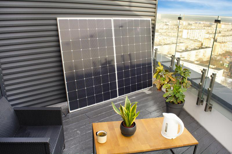 Zwei Sonnenkollektoren auf einem Balkon mit Pflanzen und Stadtblick im Hintergrund. Sonniger Tag.