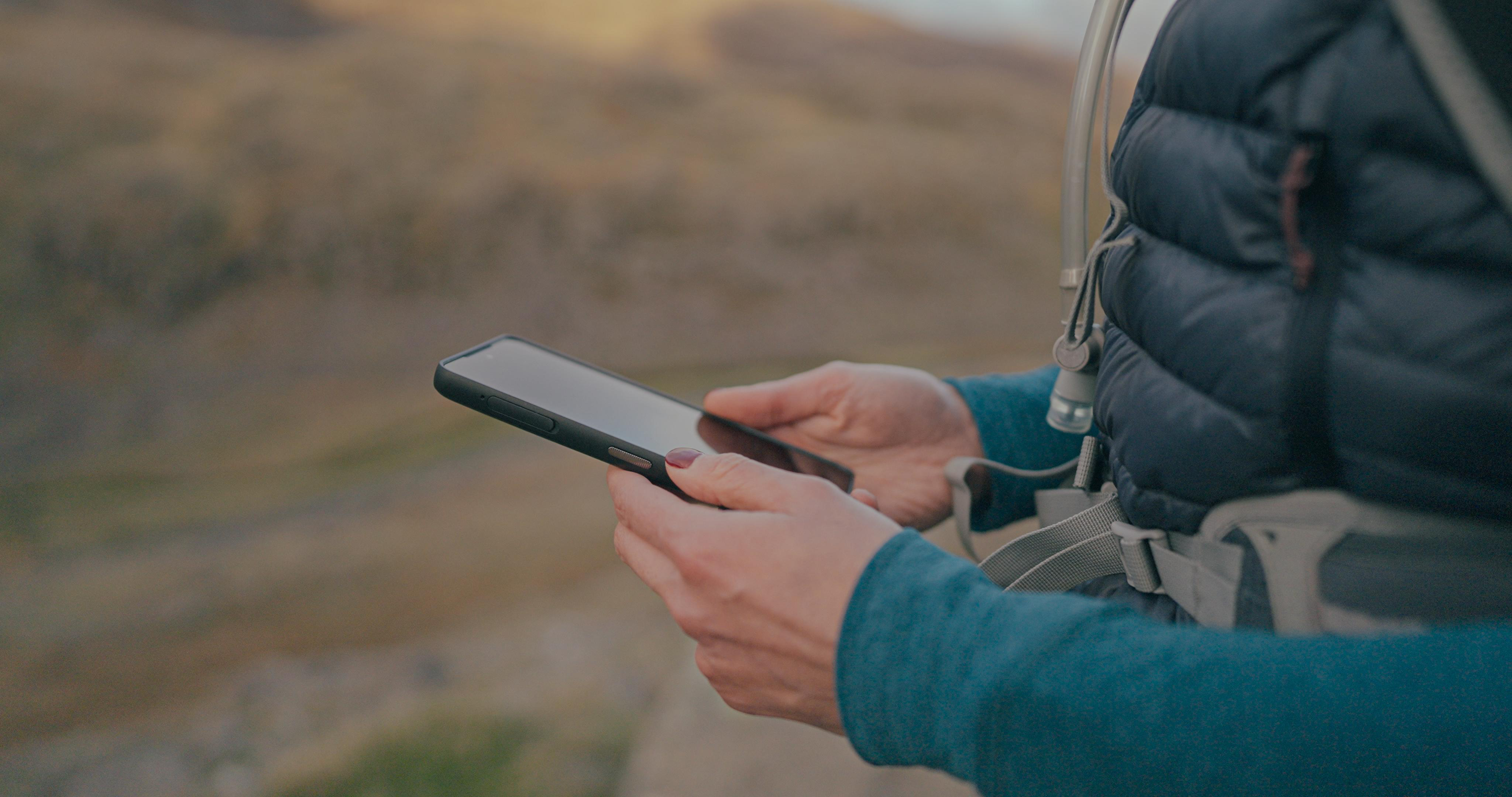 Eine Person hält ein Smartphone und benutzt es im Freien.