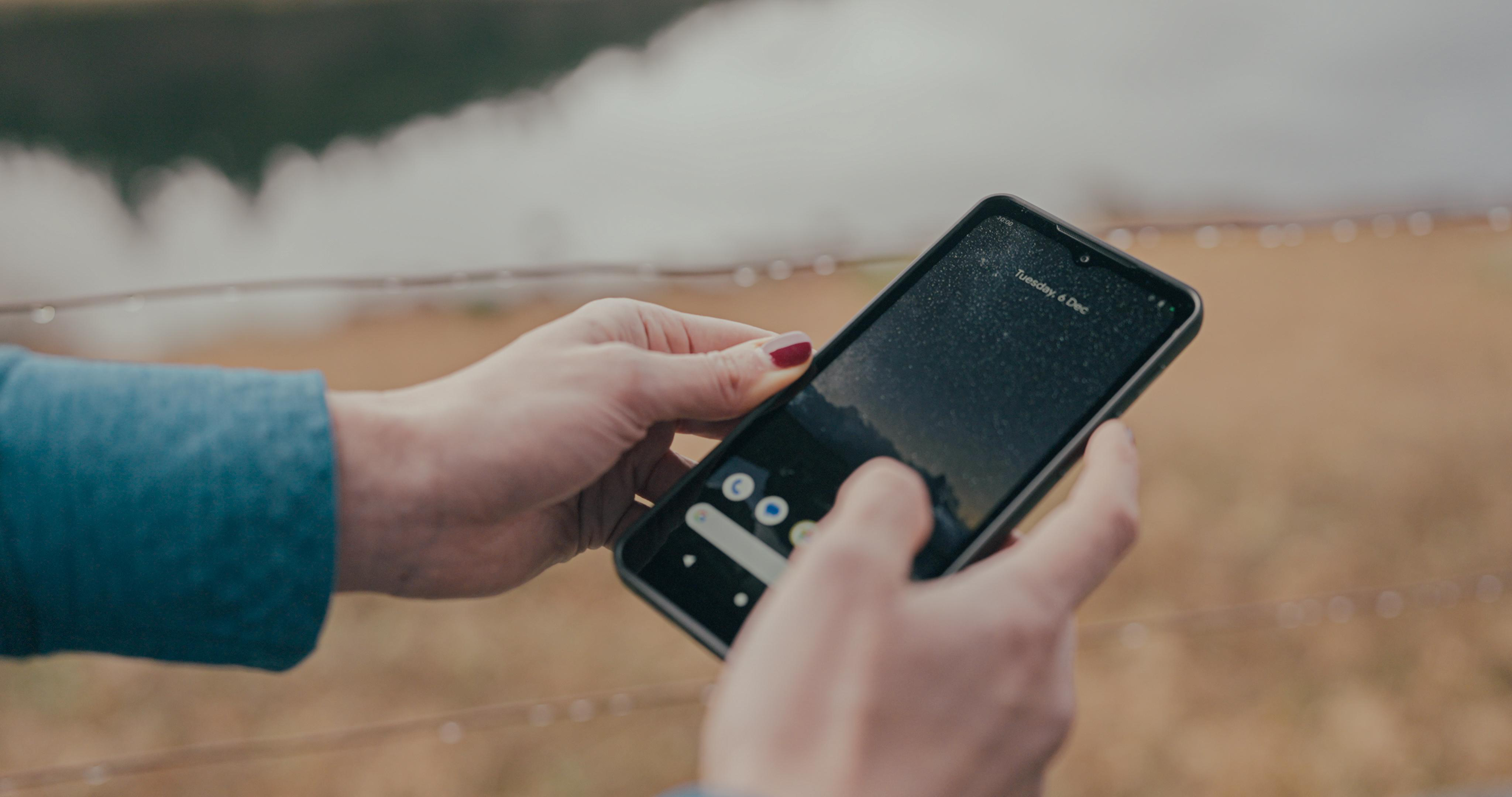 Hände einer Person, die ein schwarzes Smartphone mit einer Benutzeroberfläche halten.