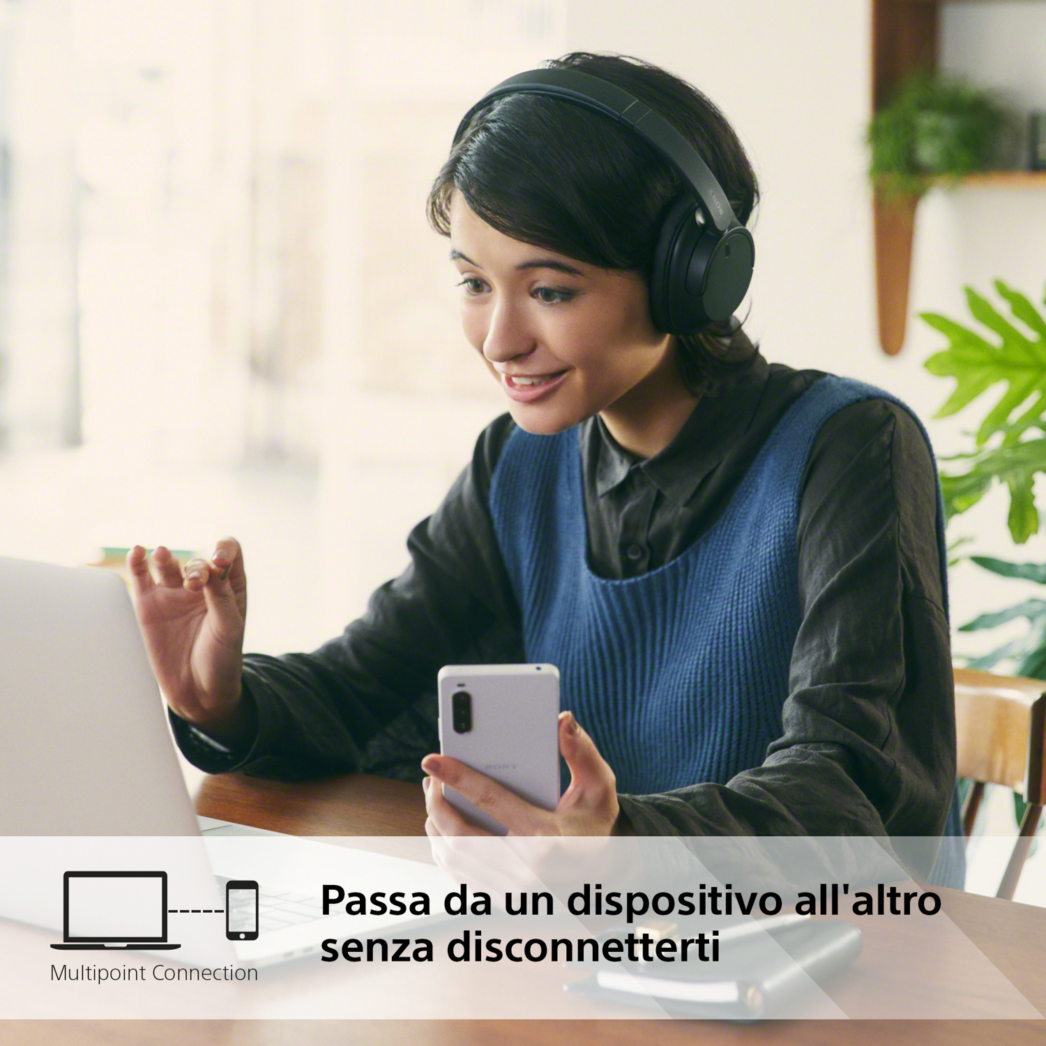 Una donna sorride, usa un laptop e uno smartphone, e indossa le cuffie.