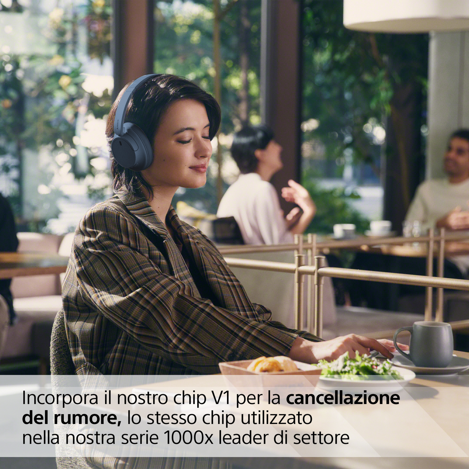 Donna in un ristorante con le cuffie, che guarda un piatto di cibo, con uno sfondo sfocato.