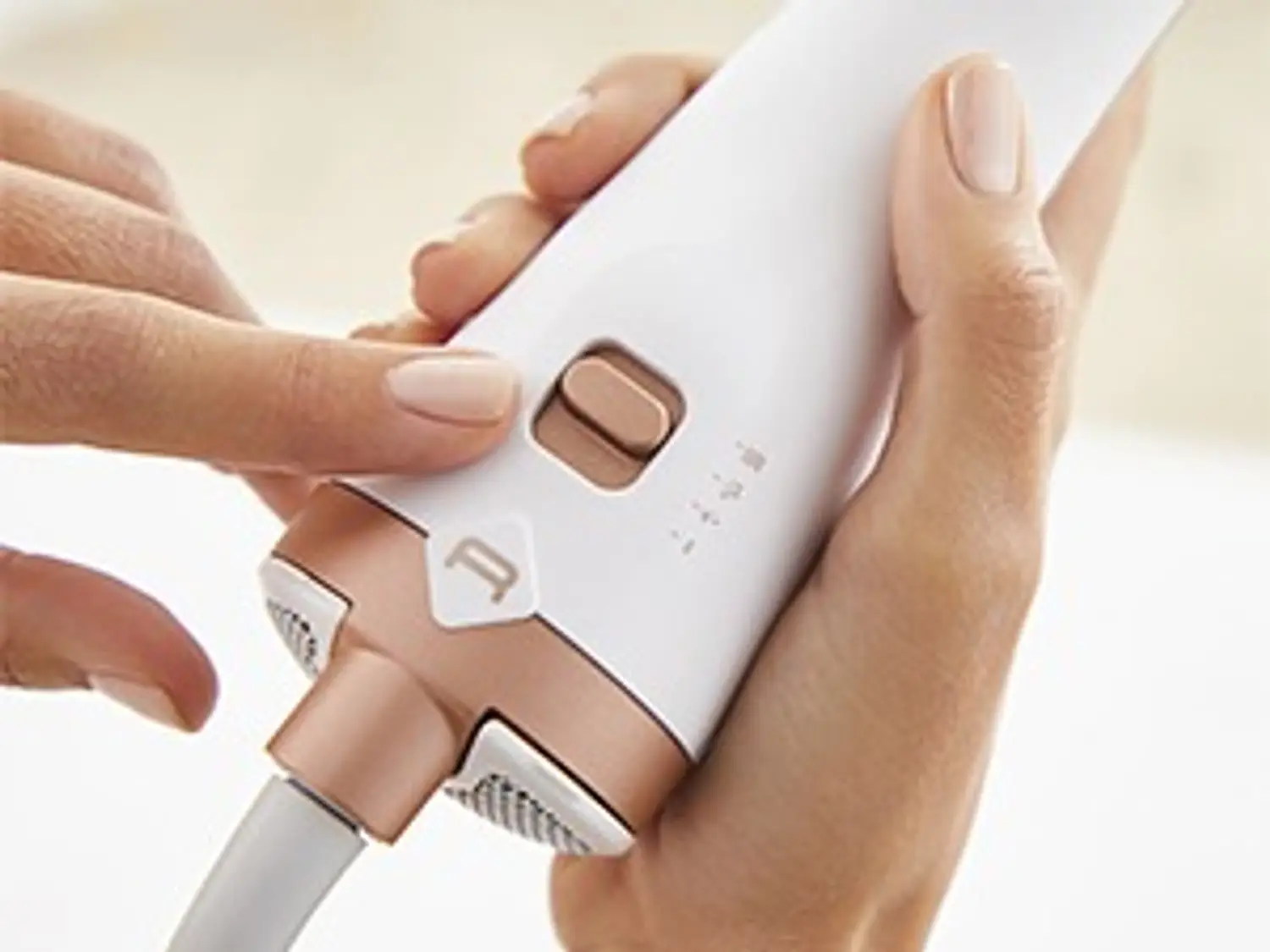 Gros plan d'une main appuyant sur un bouton d'un styler capillaire blanc et or rose.