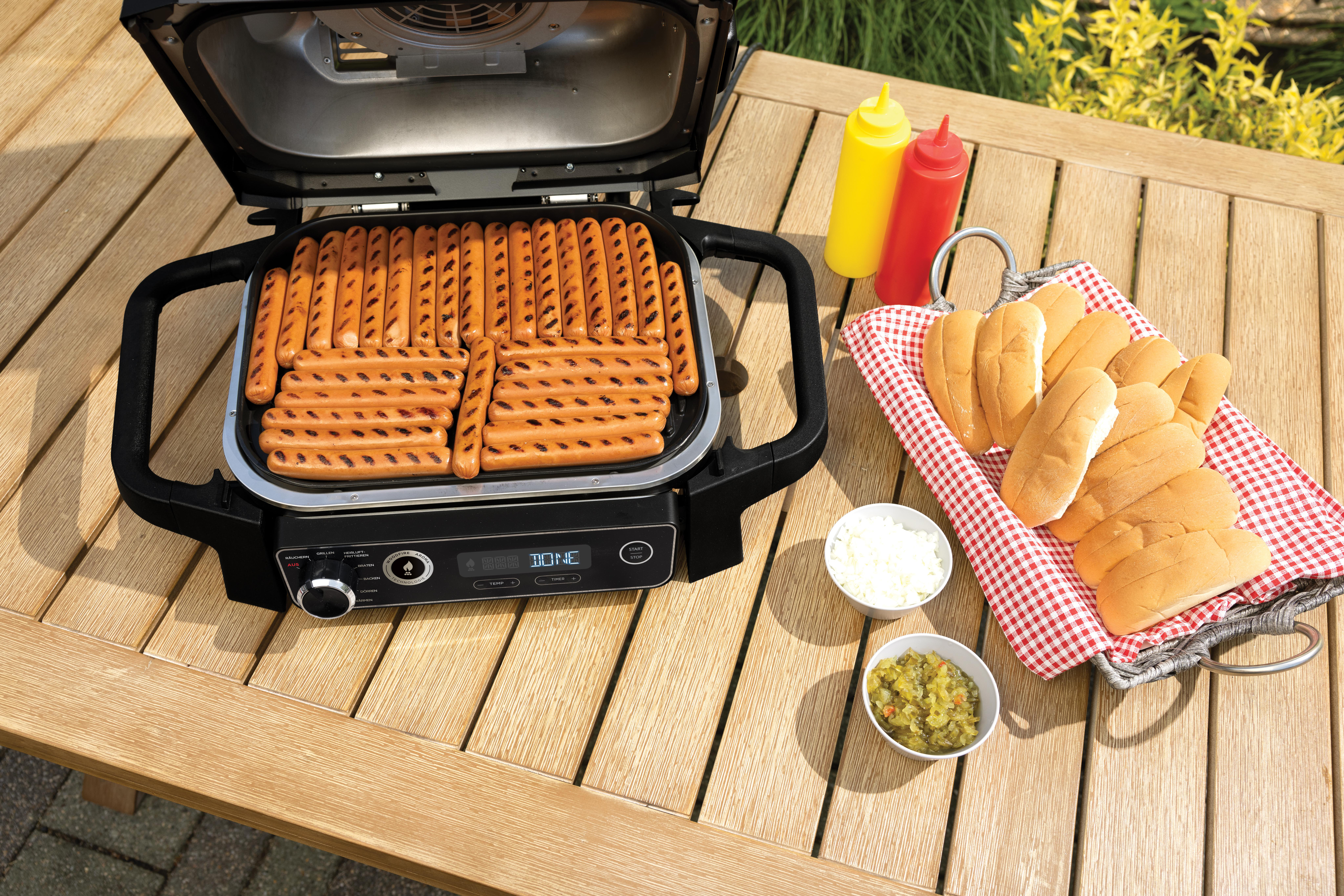 Würstchen auf einem Außengrill mit Gewürzen und Brötchen.