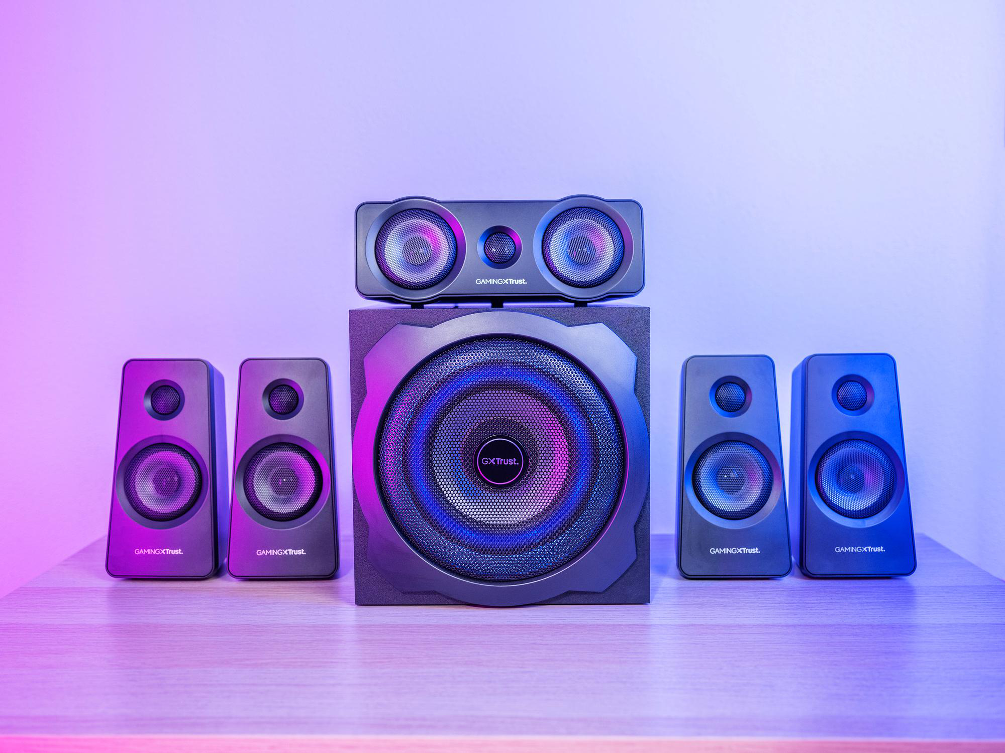 Ein Gaming-Lautsprechersystem mit Subwoofer und fünf Satelliten vor einer lilafarbenen und blauen Wand.