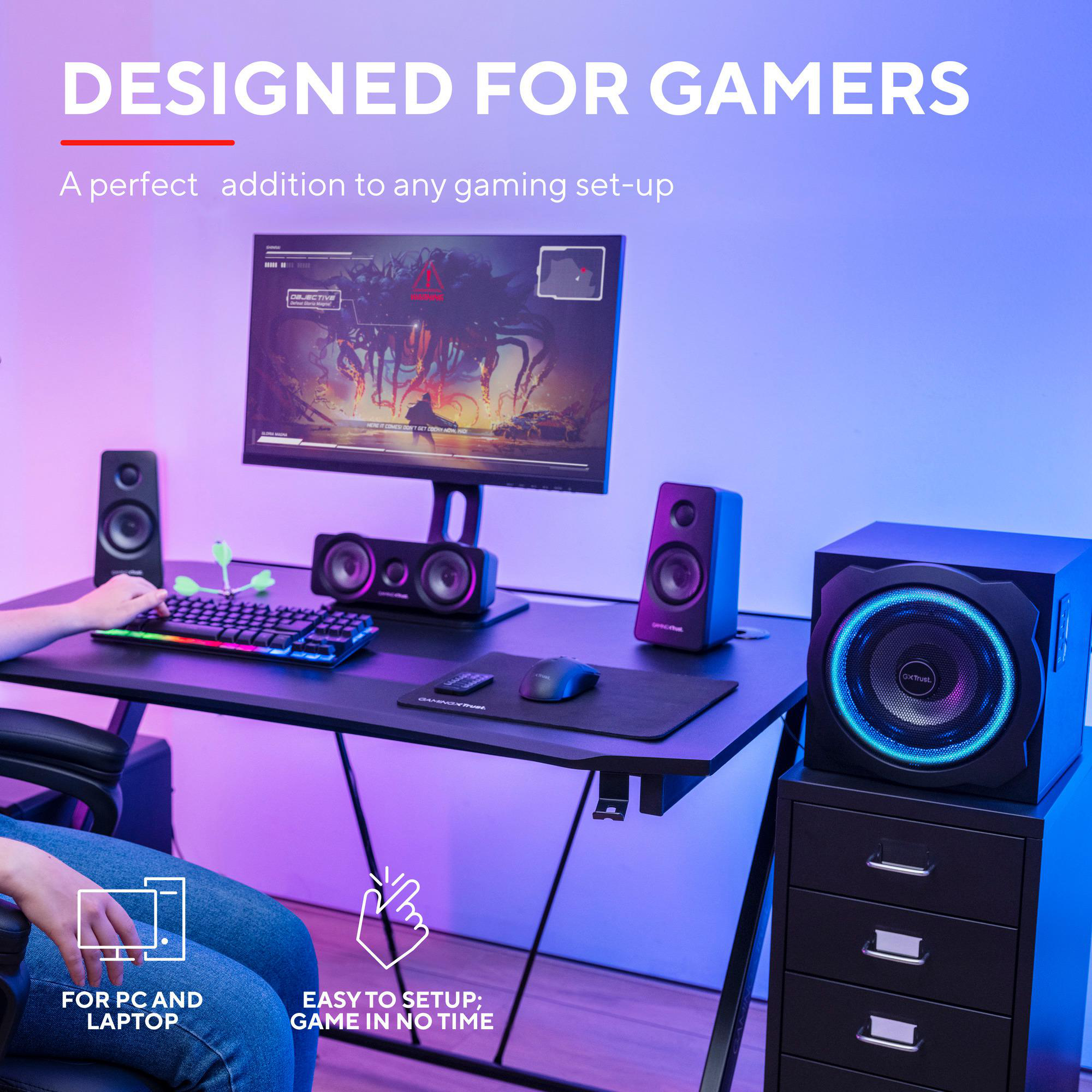 Gaming-Schreibtisch mit Monitor, RGB-Tastatur, Maus, Lautsprechern und Subwoofer. Text: Designed for gamers.
