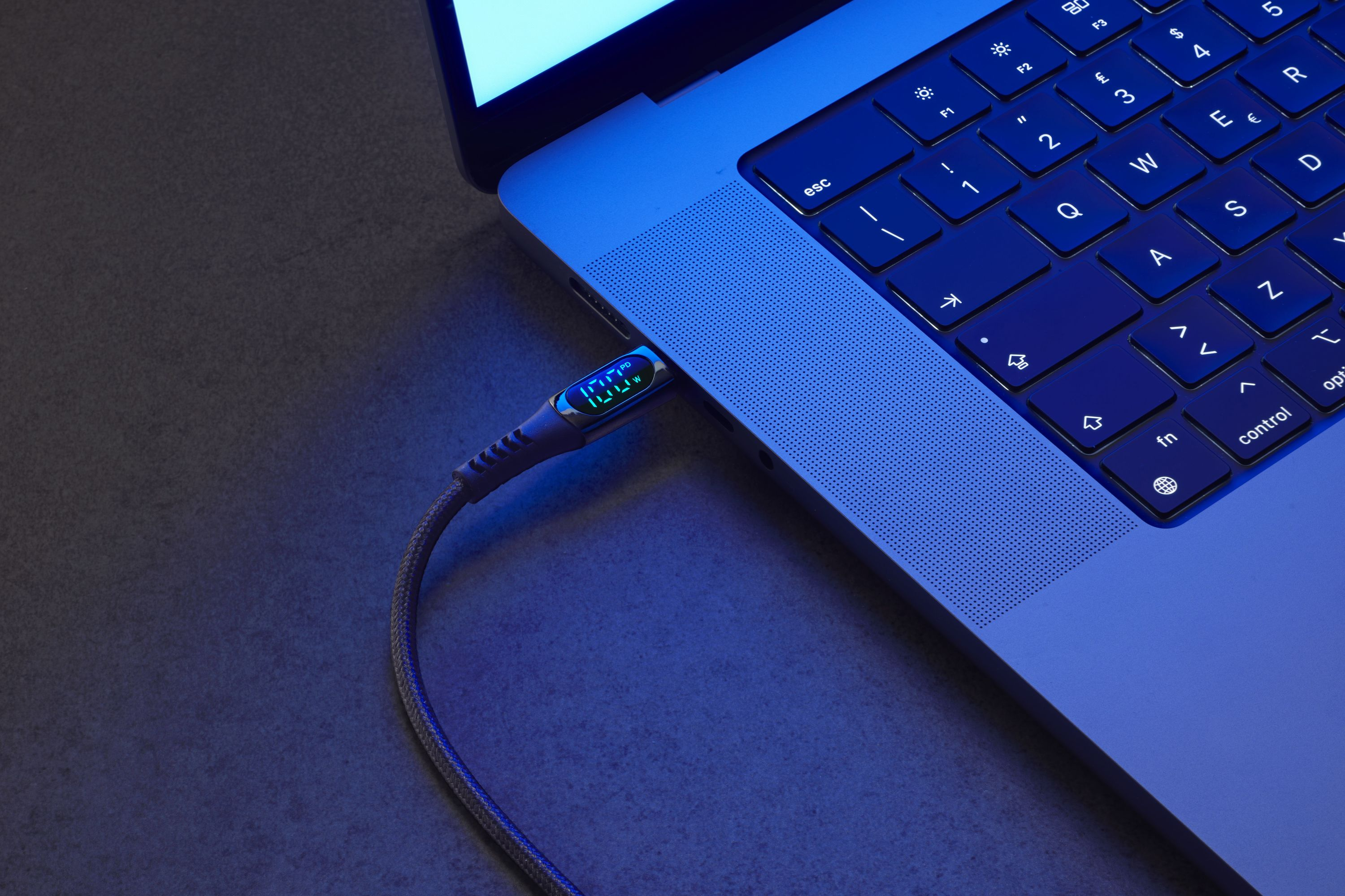 Una laptop conectada a un cable de carga, con una pantalla digital en el cable.