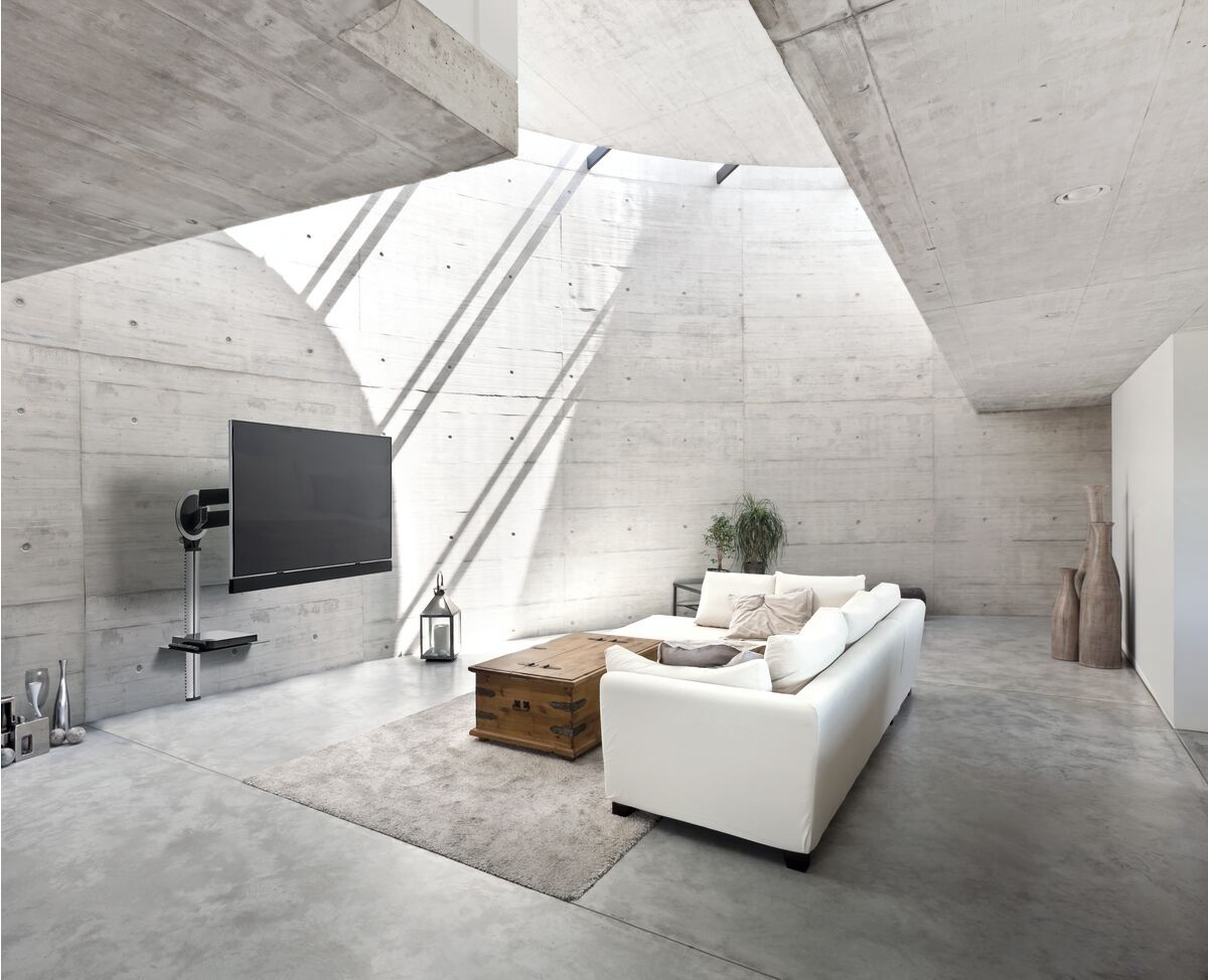 Salon moderne avec murs en béton, TV, canapé blanc et table en bois.