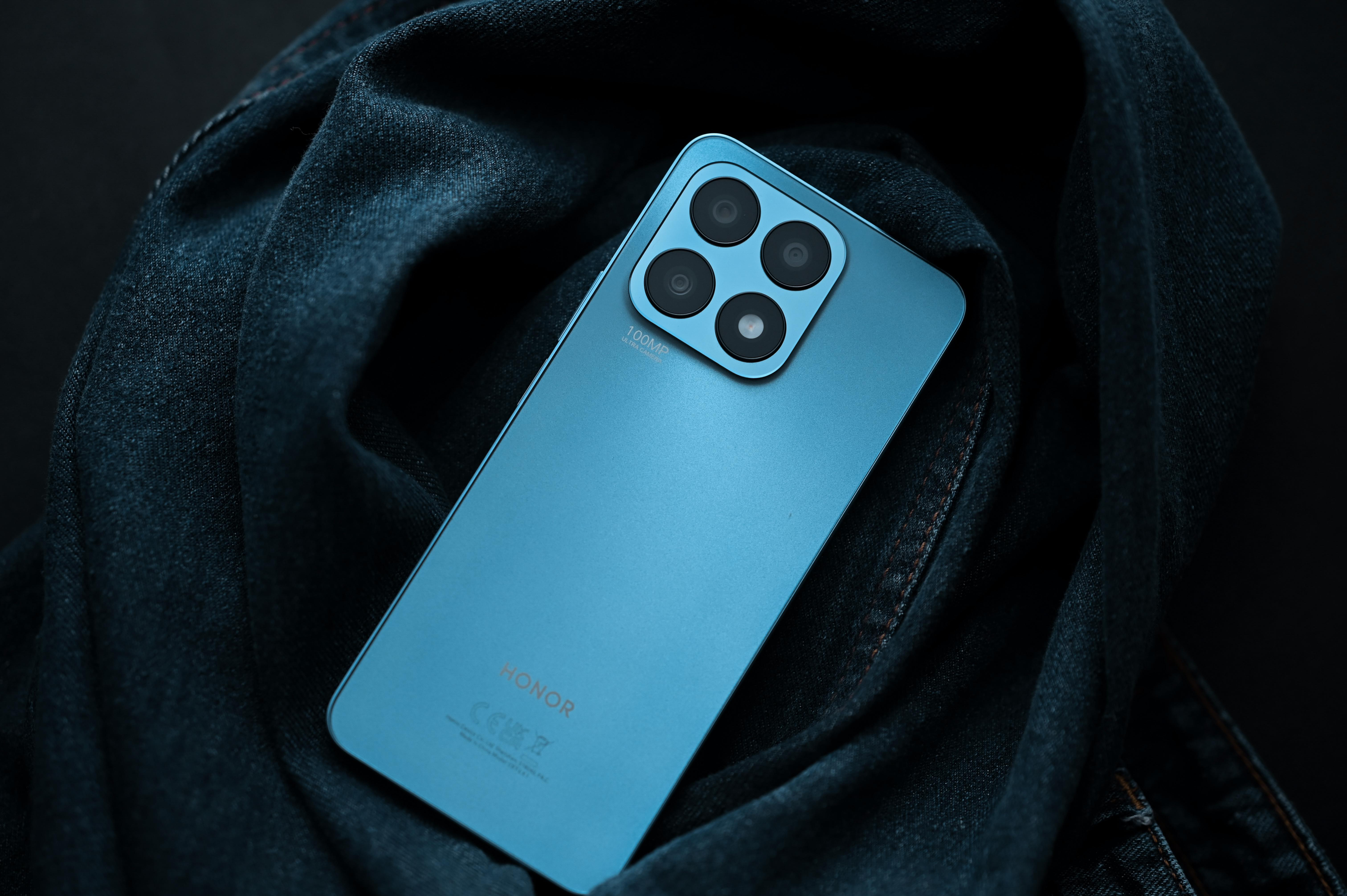 Ein blaues Smartphone auf einem dunkelblauen Jeansstoff. Das Telefon hat vier Rückkameras.