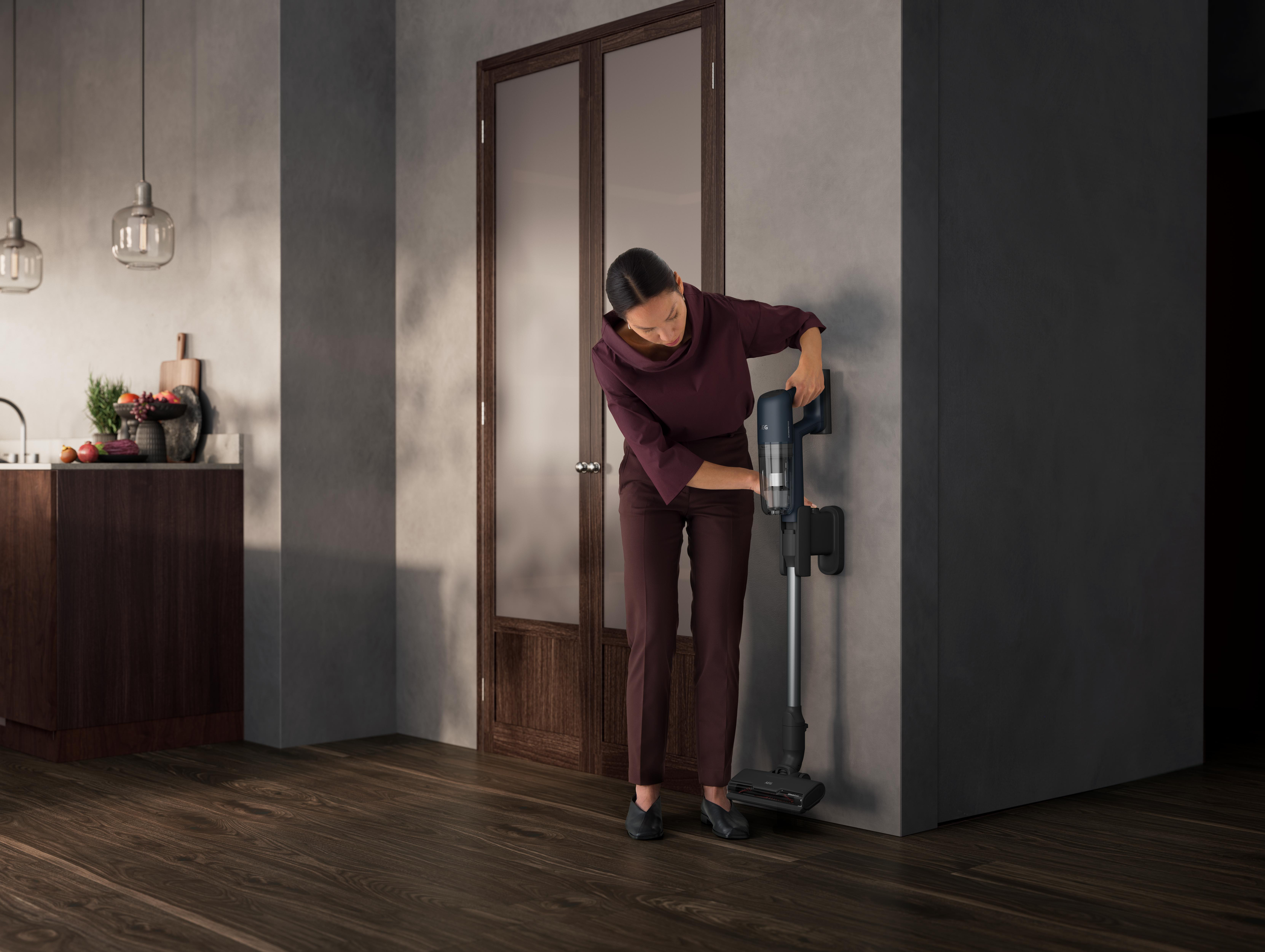 Frau, die einen Staubsauger wieder auf seine an der Wand montierte Ladestation stellt.