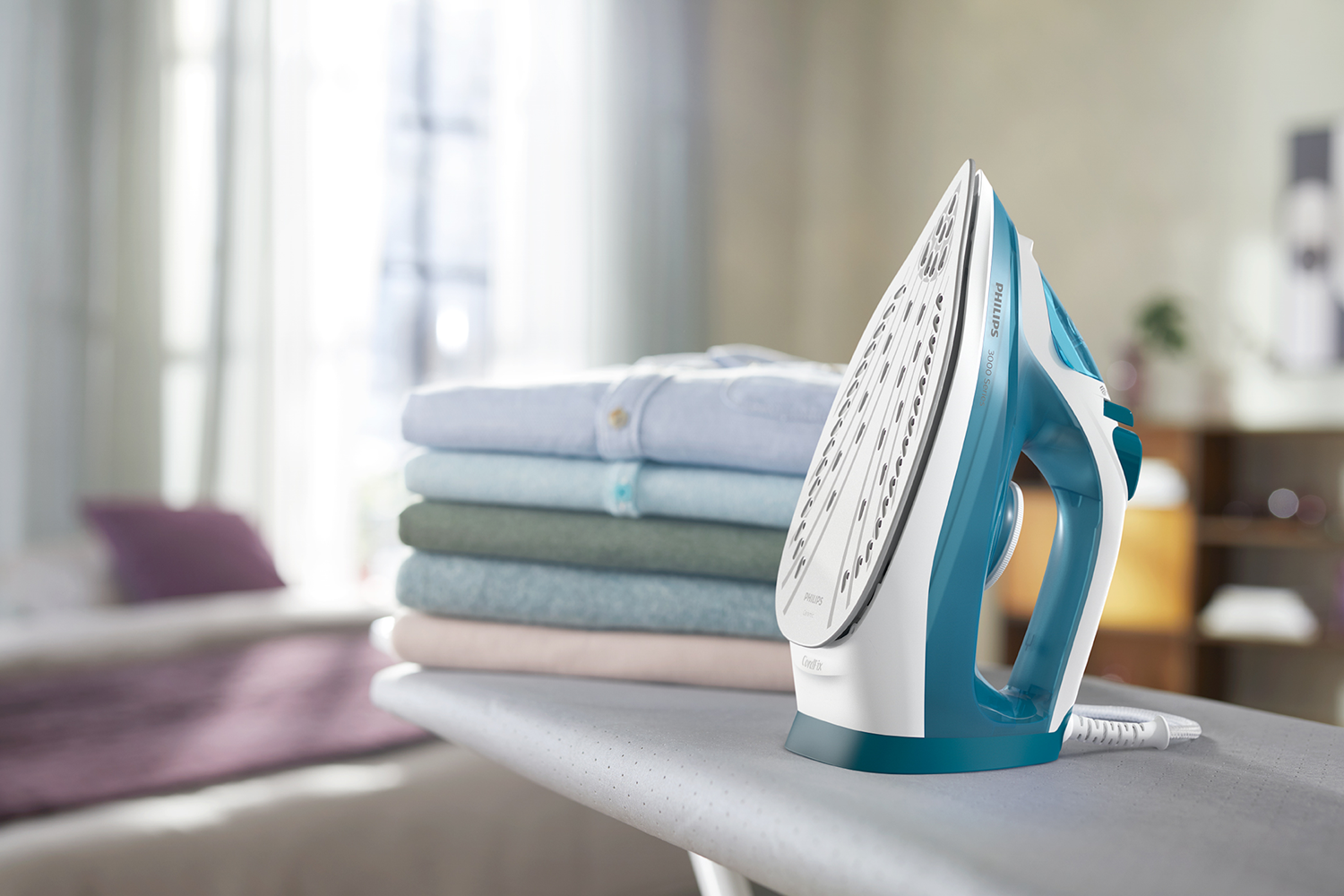 Ironing board with iron and folded shirts, window in background.