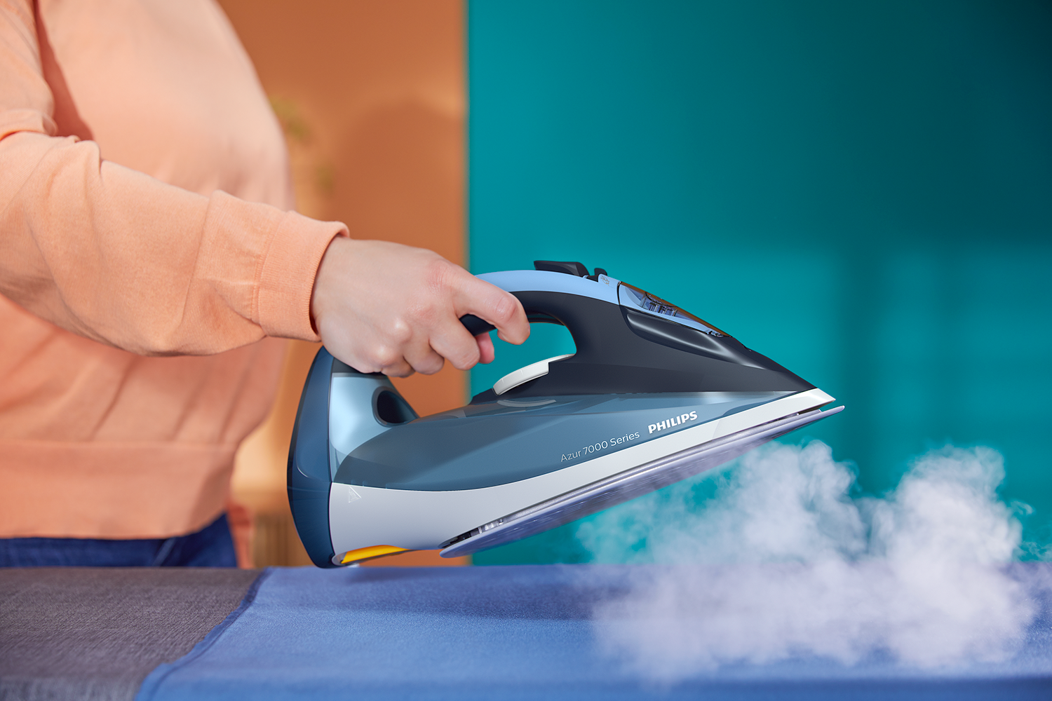 Person ironing a blue cloth with a blue and gray iron; steam visible.