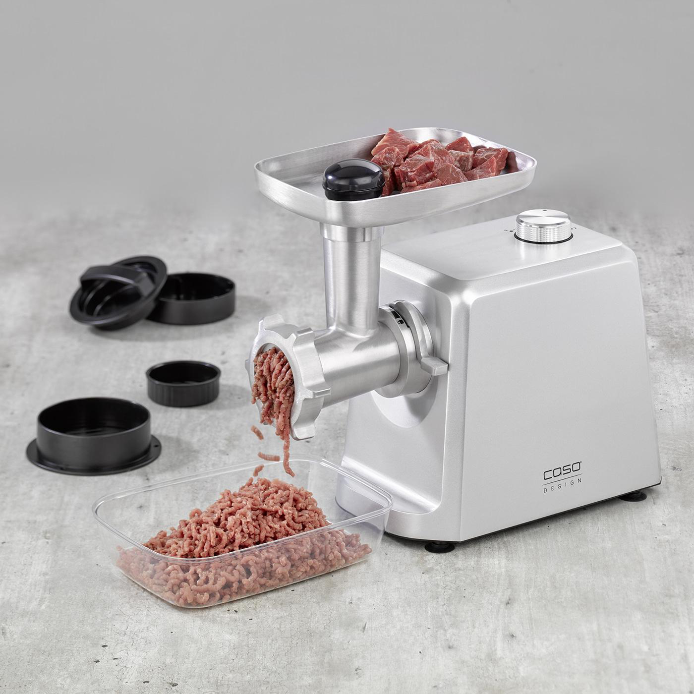 Silberner Fleischwolf mit verarbeitetem Fleisch. Eine Schüssel mit Hackfleisch und Teile daneben.
