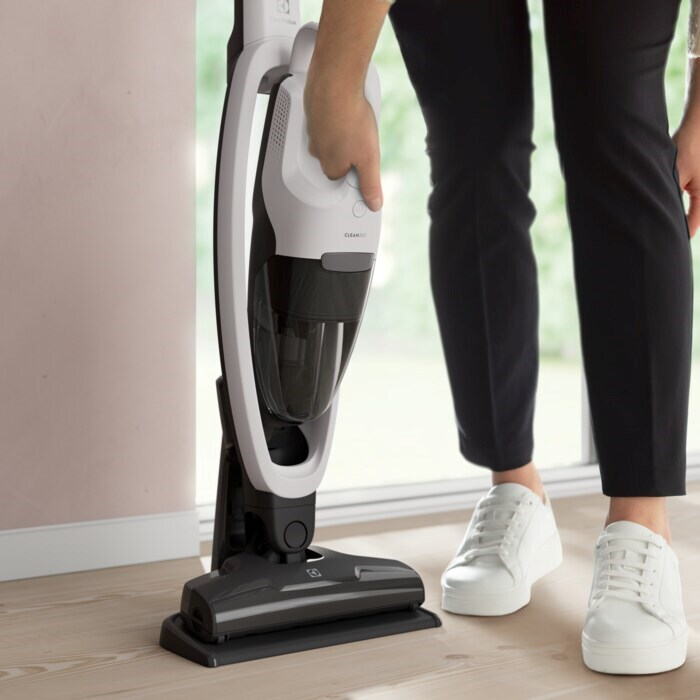 Egy fekete nadrágos, fehér cipős nő egy fehér-szürke Electrolux porszívót tart.