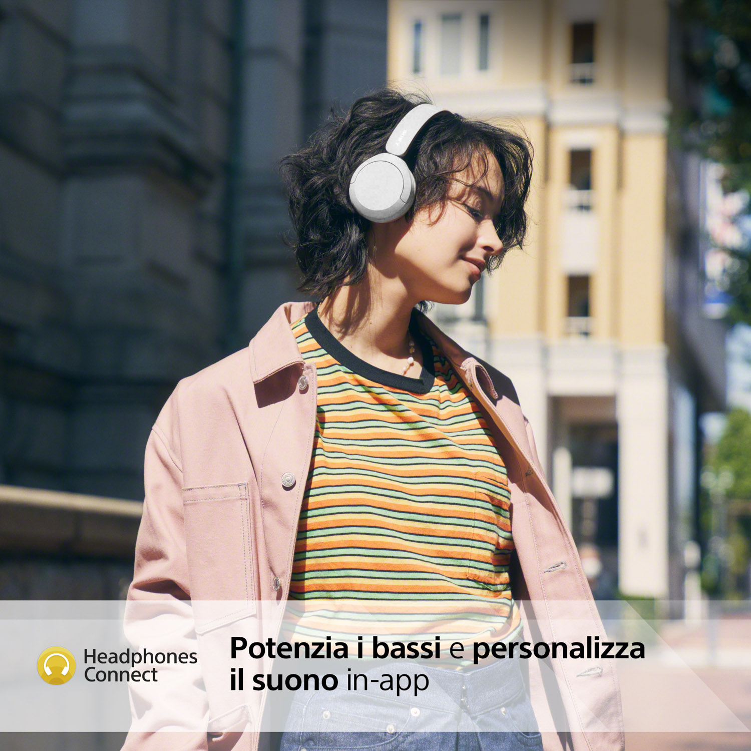 Una giovane donna con cuffie bianche, in piedi all'aperto, sorridente.
