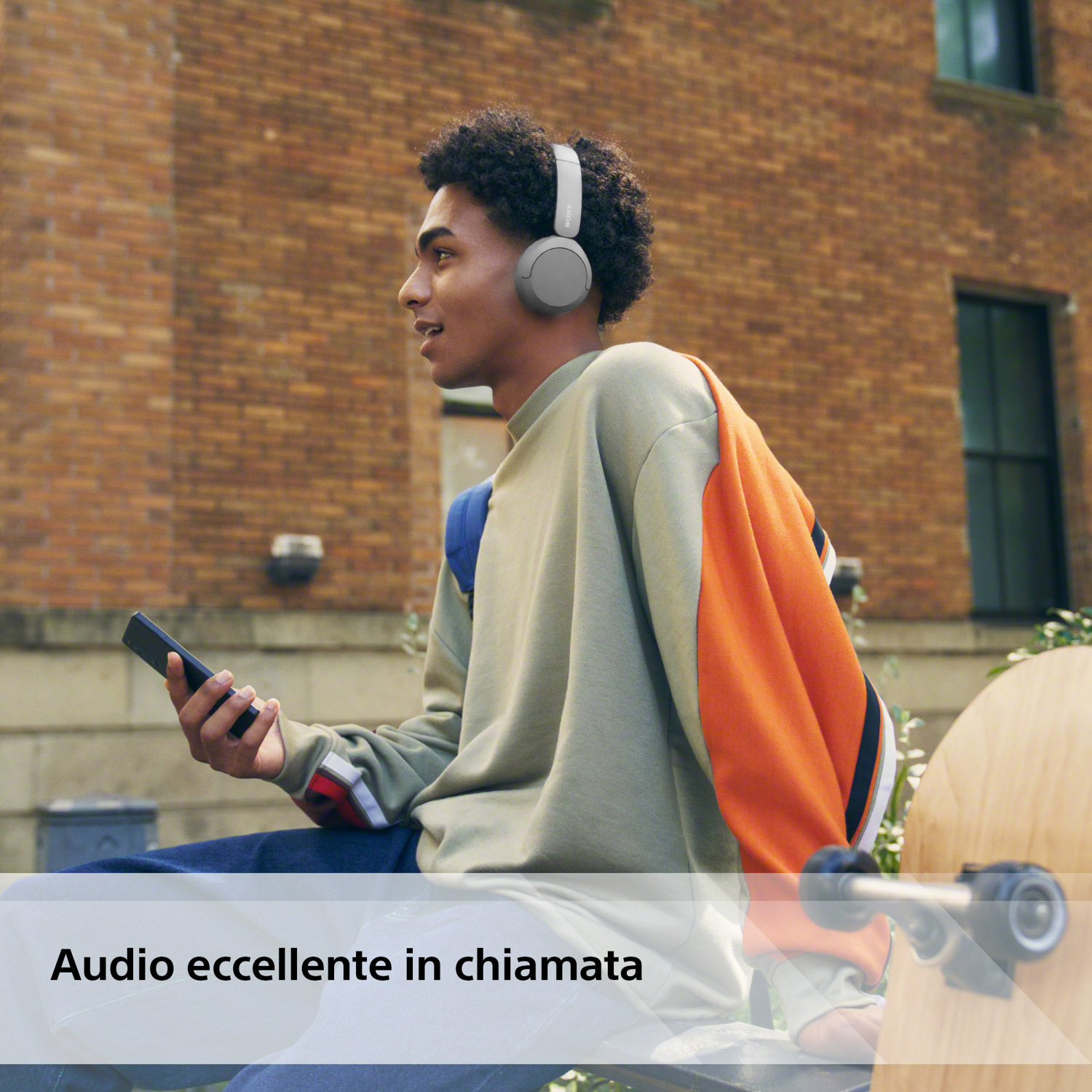 Un uomo con cuffie e telefono, seduto fuori davanti a un edificio.