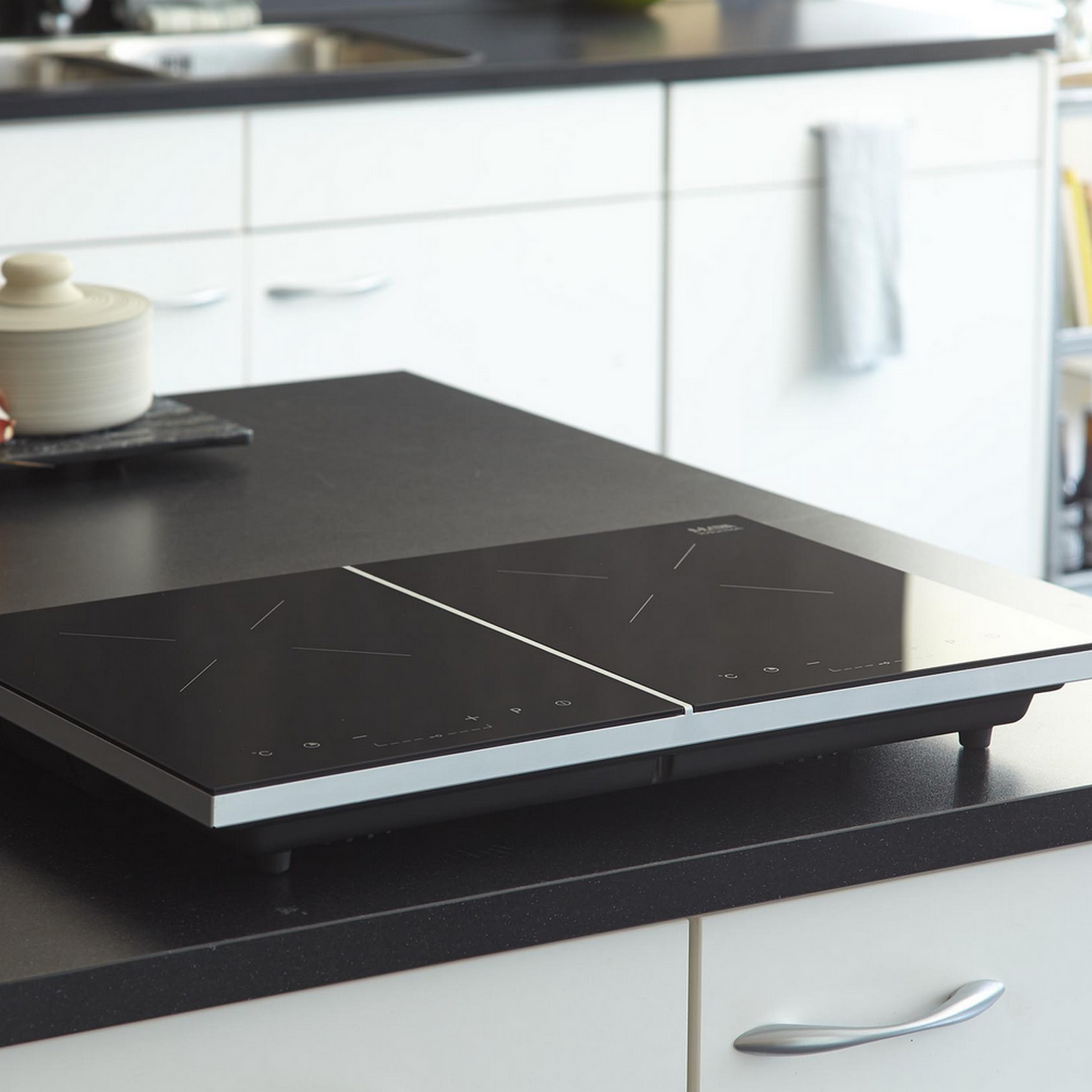 Black cooktop with two cooking zones. It's on a black countertop in a kitchen.