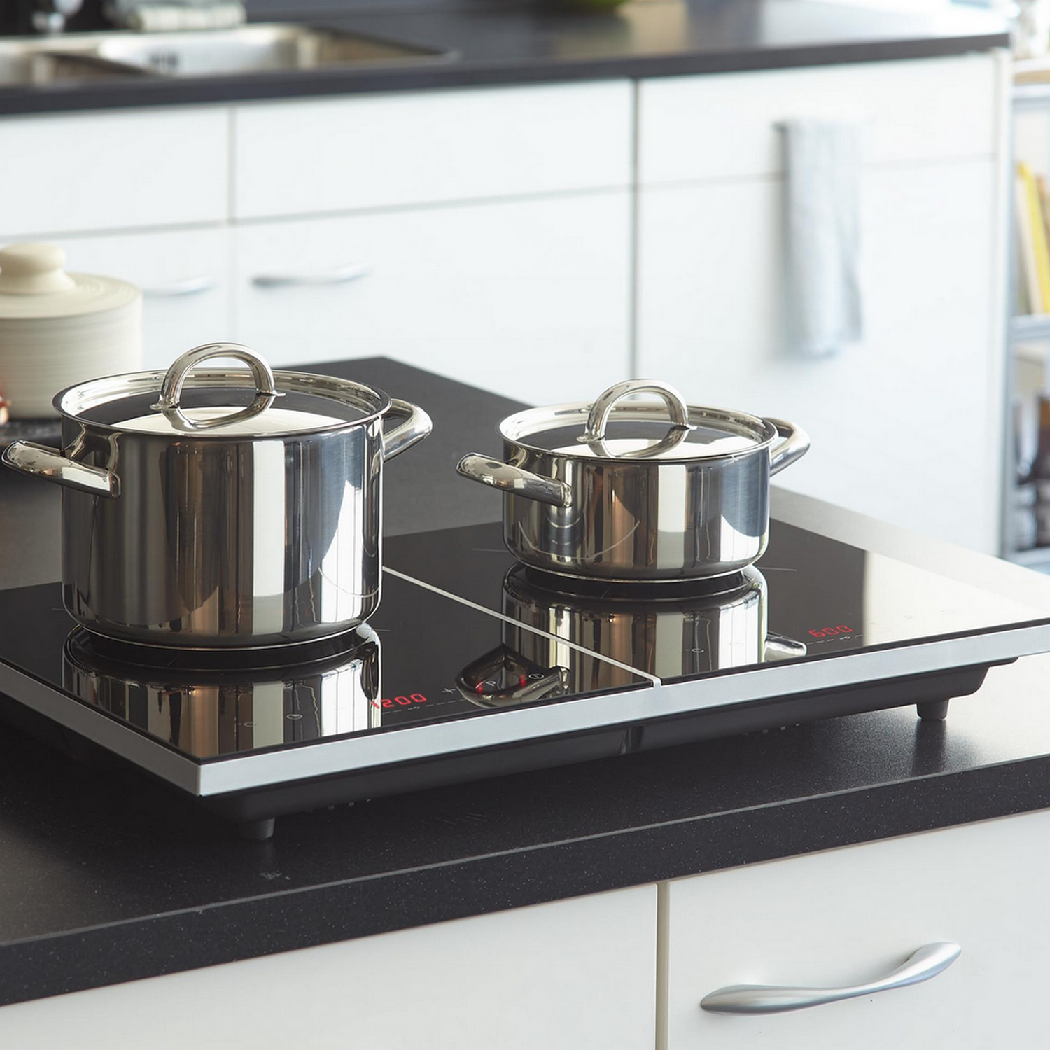 Two stainless steel pots on an induction cooktop, set on a black countertop.