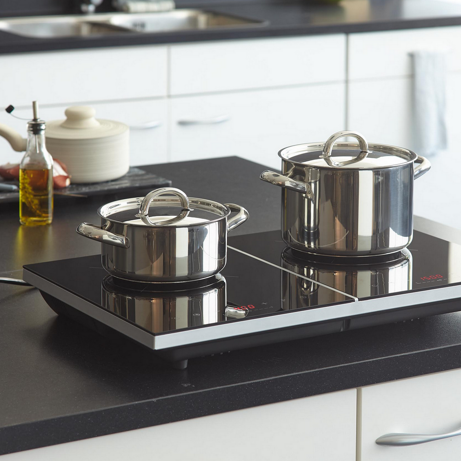 Two stainless steel pots on an induction cooktop, with a kitchen background.