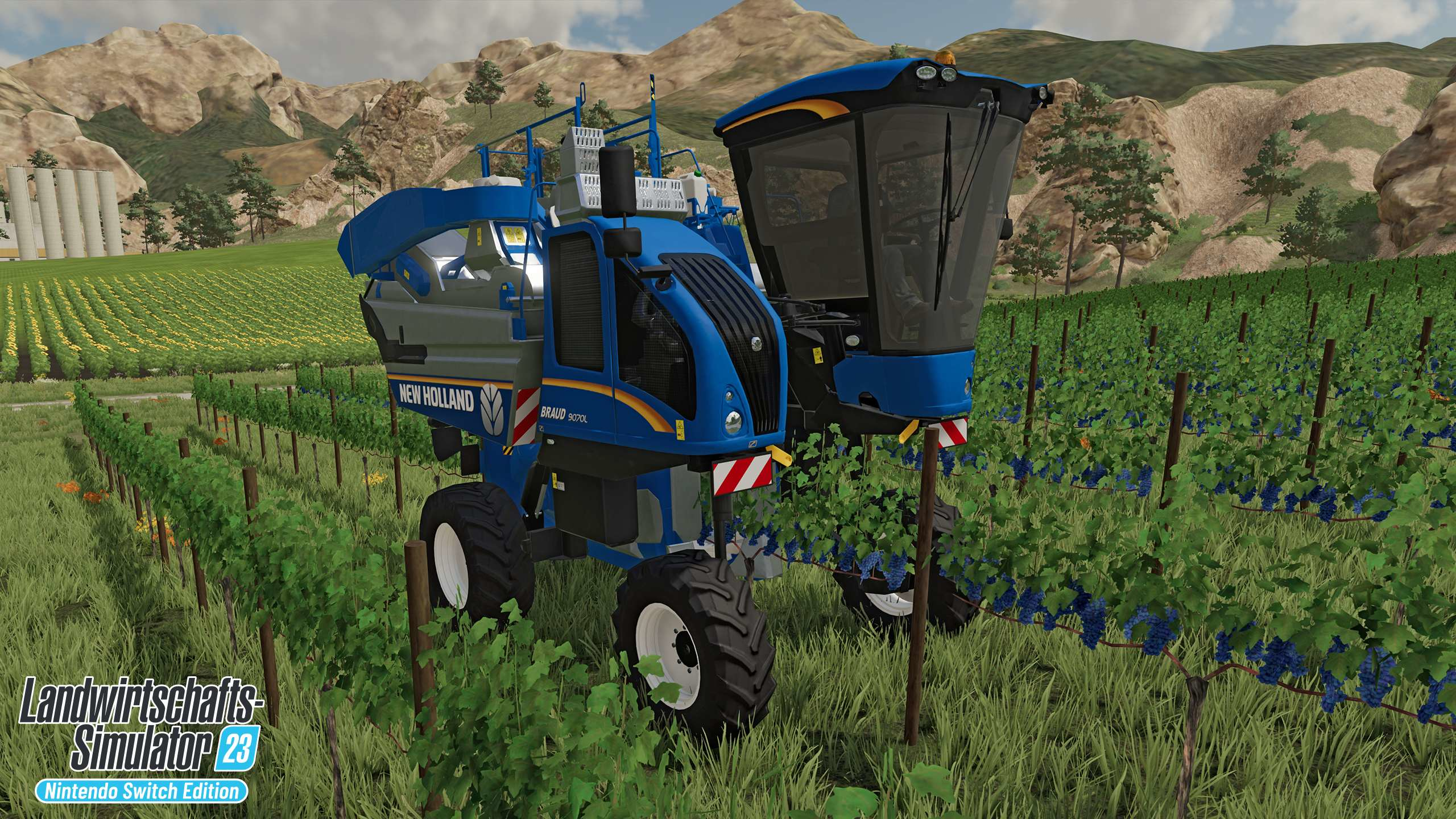Ein blau-weißer New Holland Traubenernter in einem Weinberg, mit blauem Himmel und Bergen.