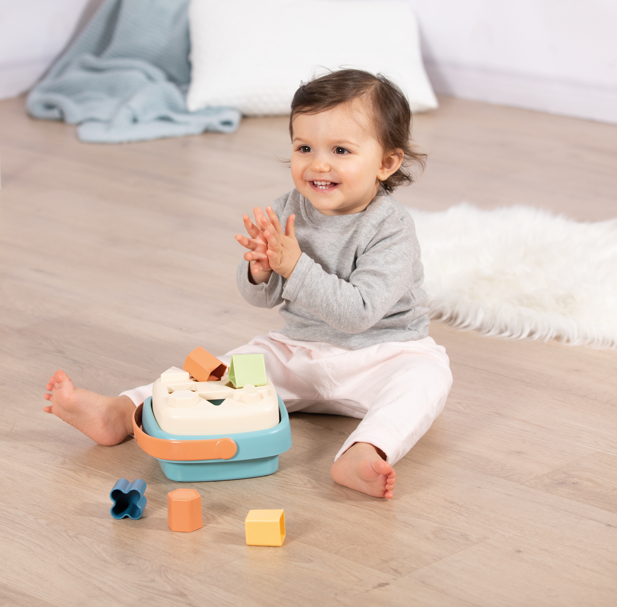 Ein Baby sitzt mit einem Formensortierer, lächelt und klatscht.