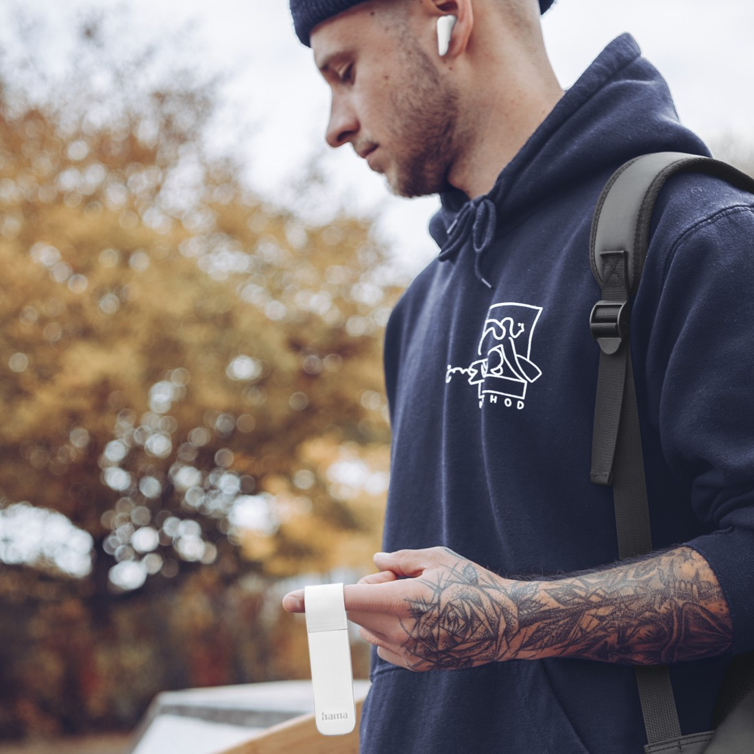 Ein Mann in einem blauen Kapuzenpullover hält ein weißes Gerät. Er hat Tätowierungen auf dem Arm.