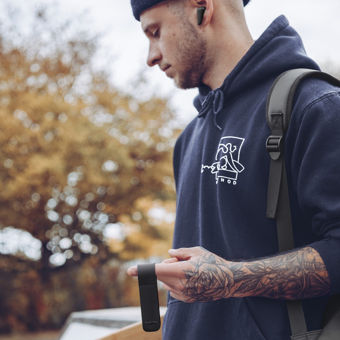 Ein Mann mit Kapuzenpullover hält ein schwarzes Objekt, Tattoo am Arm.