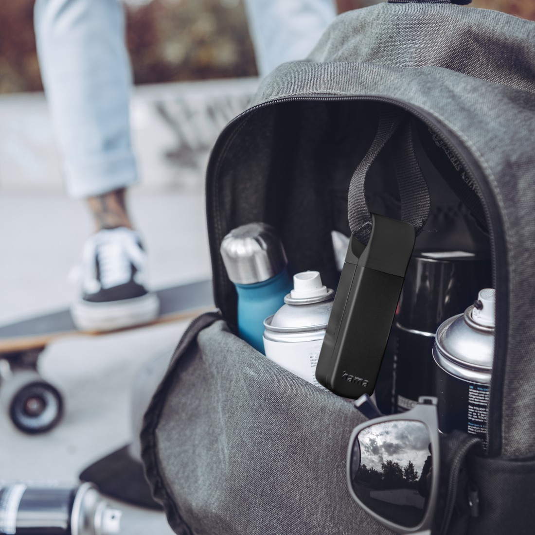Rucksack mit Sprühdosen und Zubehör, gehalten von jemandem auf einem Skateboard, Umgebung im Freien.
