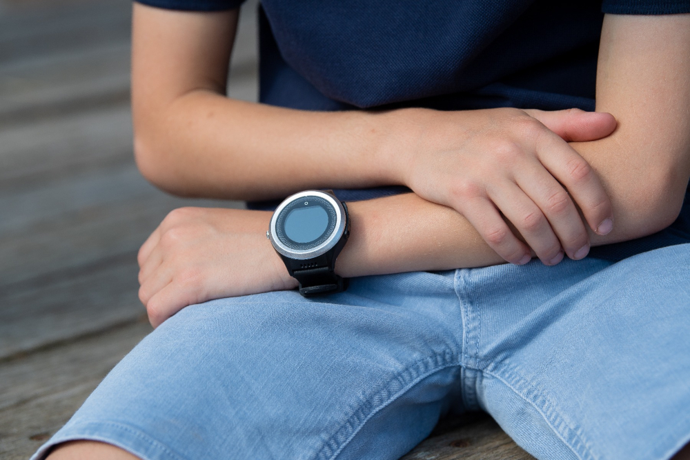 Personne portant une montre intelligente au poignet. La montre est noire avec une lunette argentée.