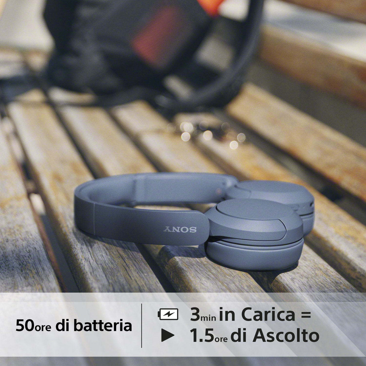 Cuffie grigie su una panchina di legno. Il testo recita '50 ore di batteria' e '3min in Carica = 1.5 ore di Ascolto'.