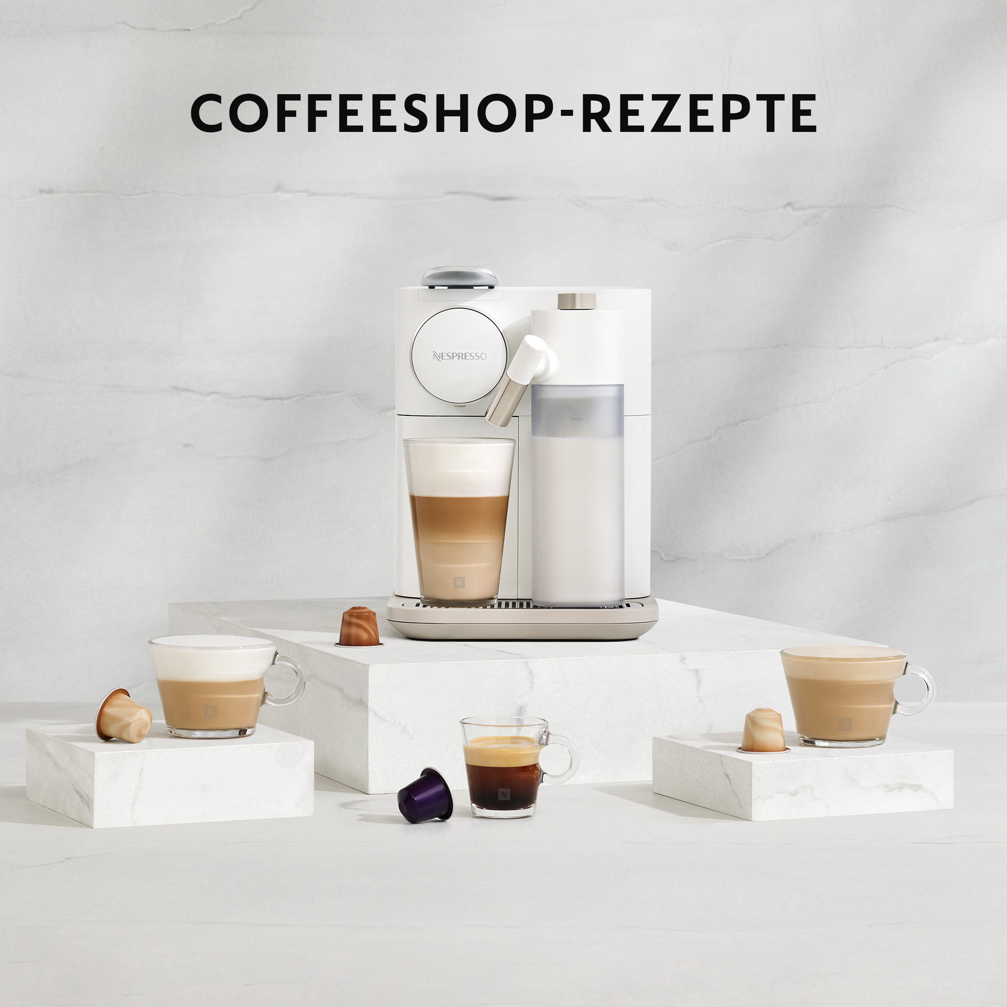Weiße Nespresso-Maschine mit Kaffeetassen und Kapseln auf weißen Marmoroberflächen.