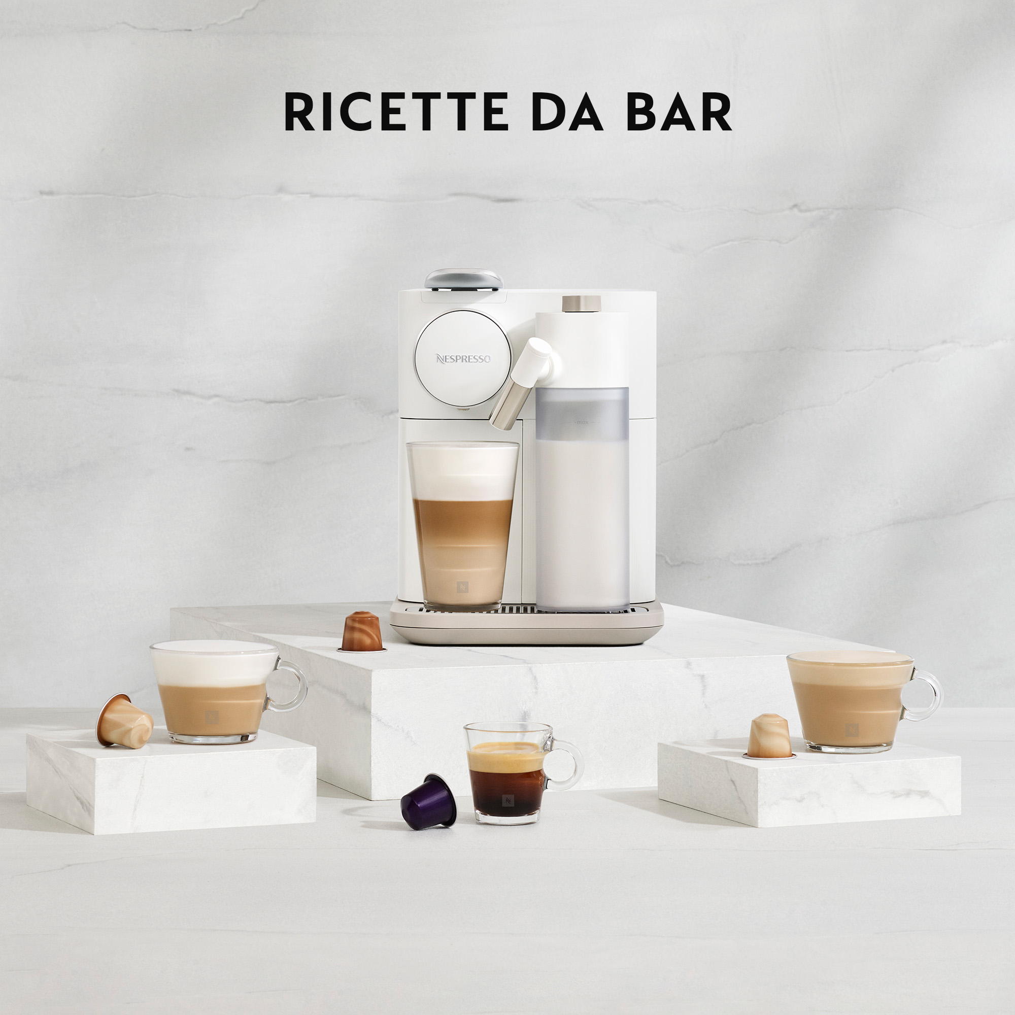 Machine Nespresso blanche avec tasses et dosettes de café sur blocs de marbre.