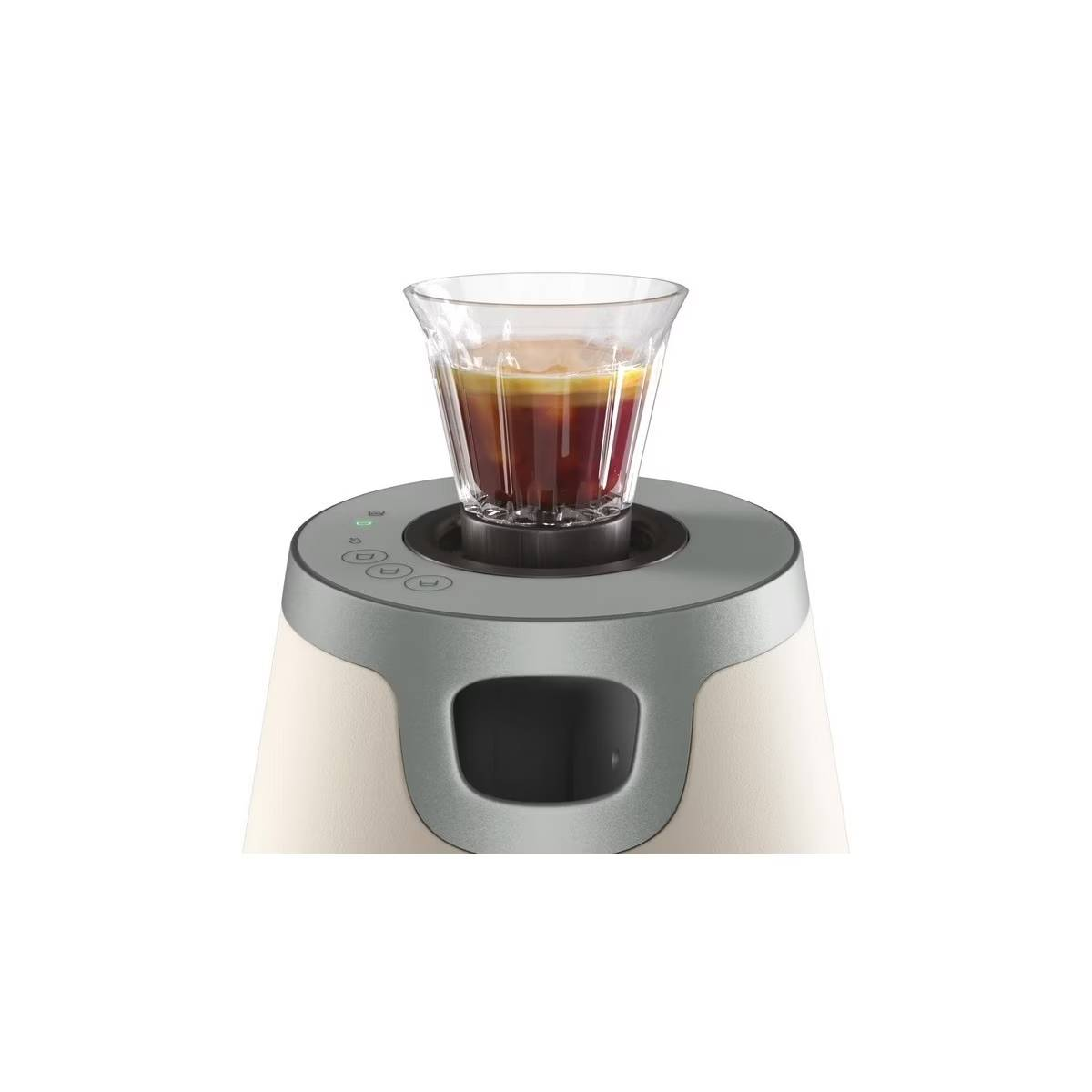 Máquina de espresso con un vaso de espresso encima, tonos beige claro y gris.