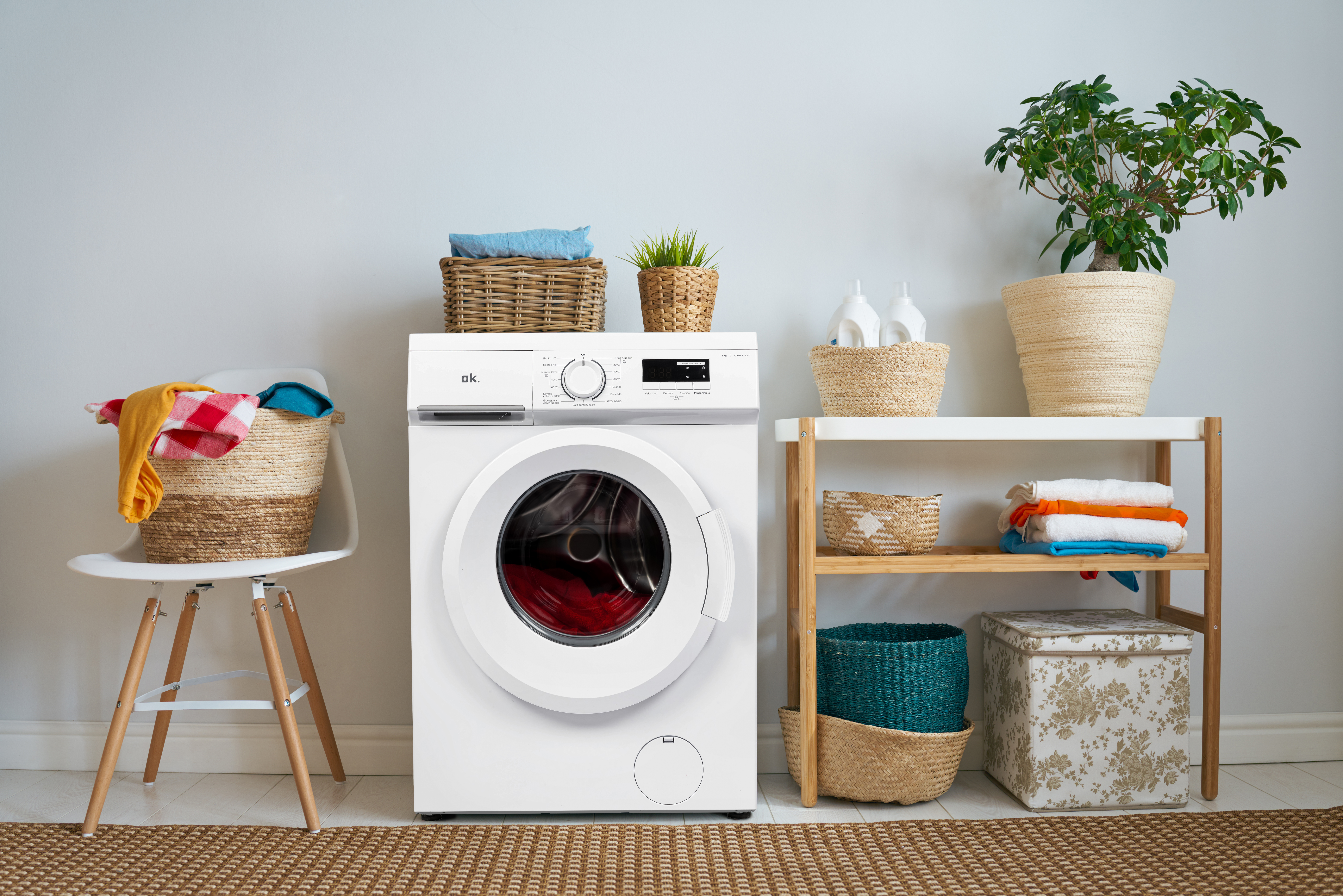 Un cuarto de lavado con una lavadora blanca, una silla y una estantería con suministros de lavandería.